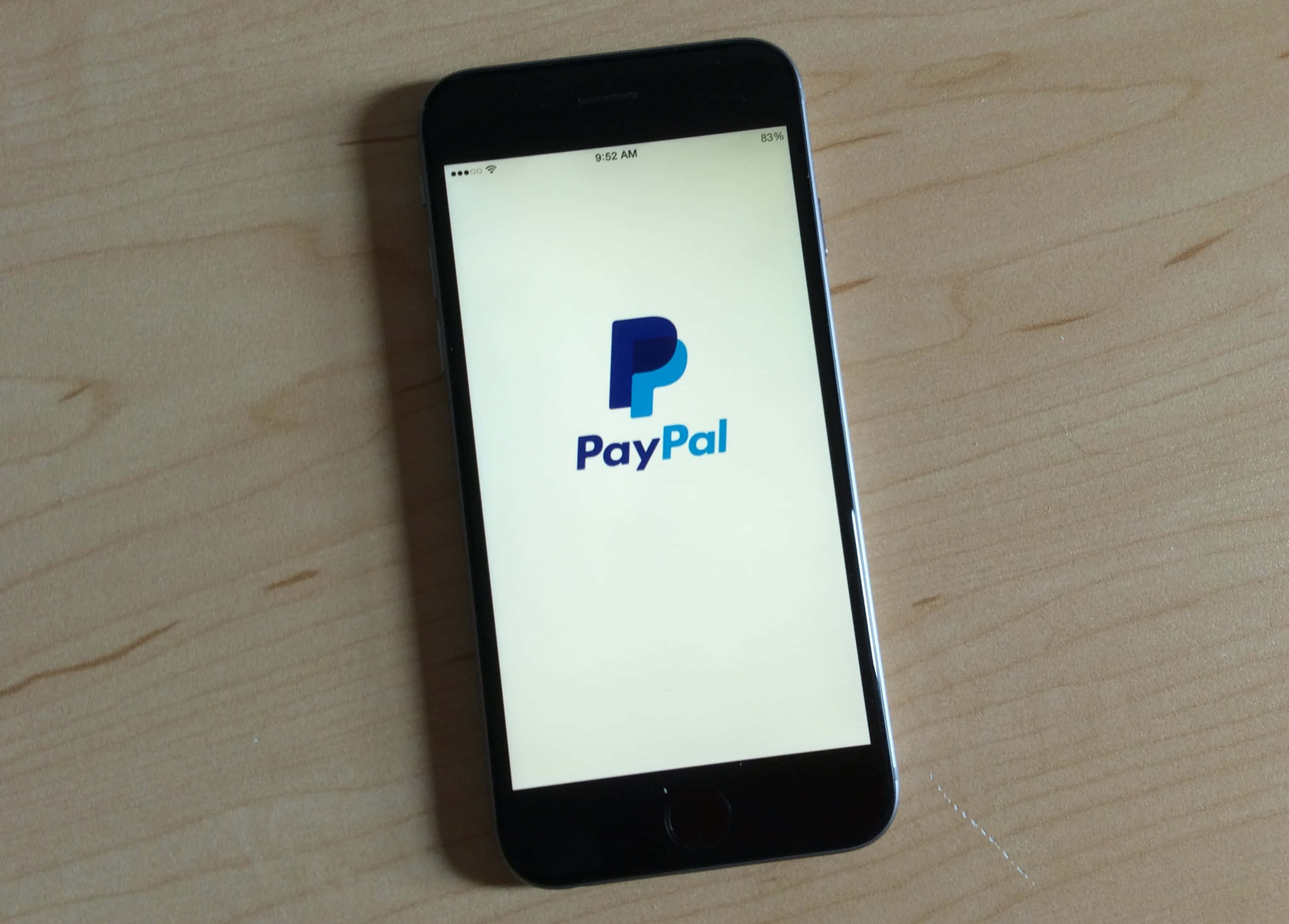 PayPal 桌布 壁紙 — 一部顯示PayPal標誌的黑色智慧型手機放在淺色木紋表面上。