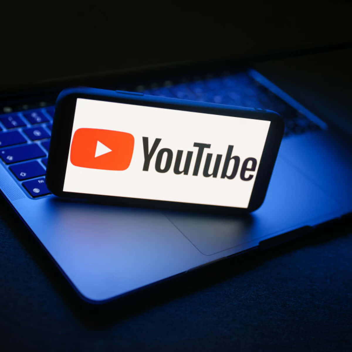 YouTube 桌布 壁紙 — 一部顯示YouTube標誌的智慧型手機放在筆記型電腦鍵盤上，處於冷藍色環境燈光下。