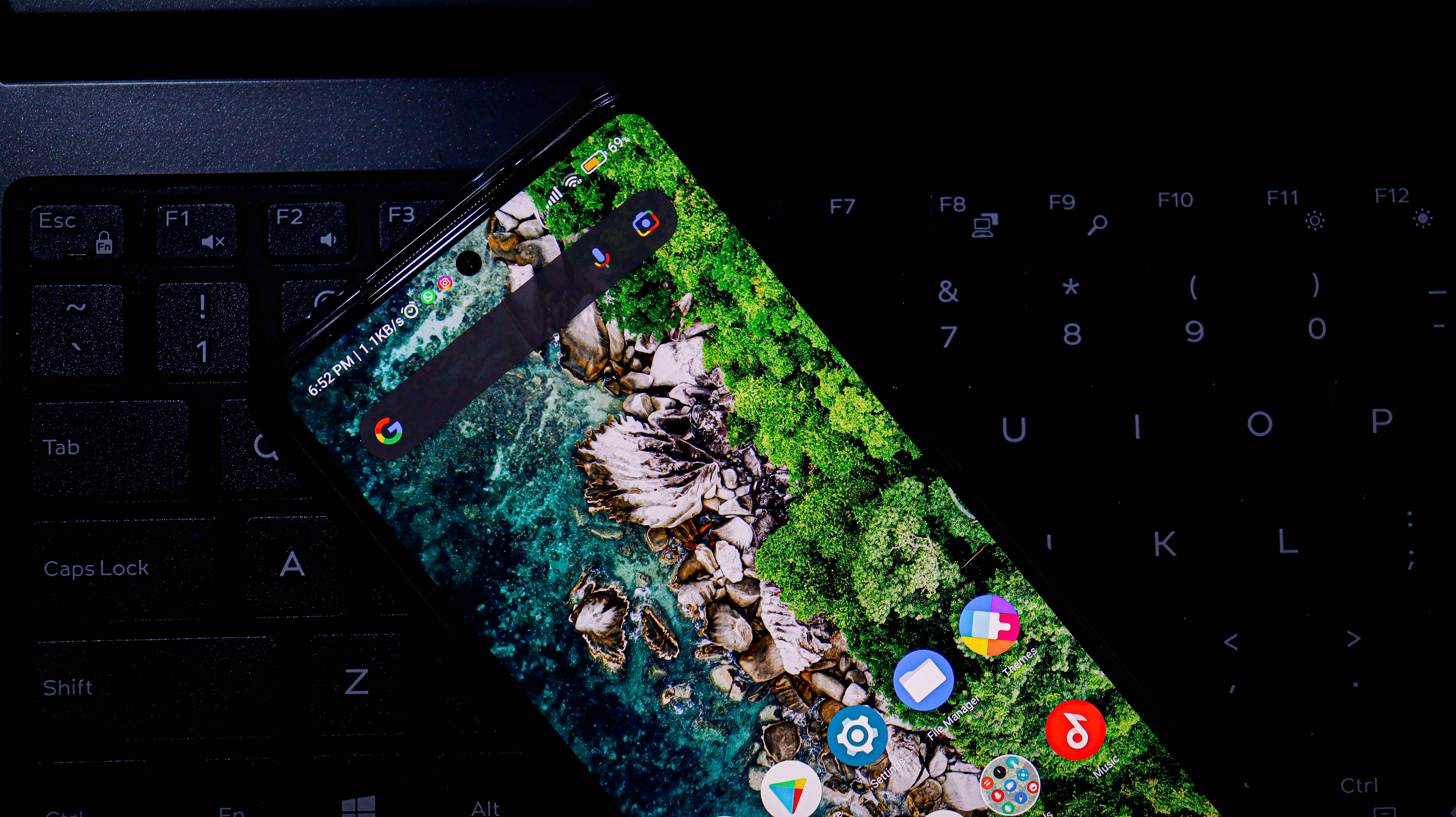 Xiaomi 桌布 壁紙 — 一部顯示充滿活力的海岸桌布的智慧型手機對角線地放在一個帶有發光按鍵的深色鍵盤上。