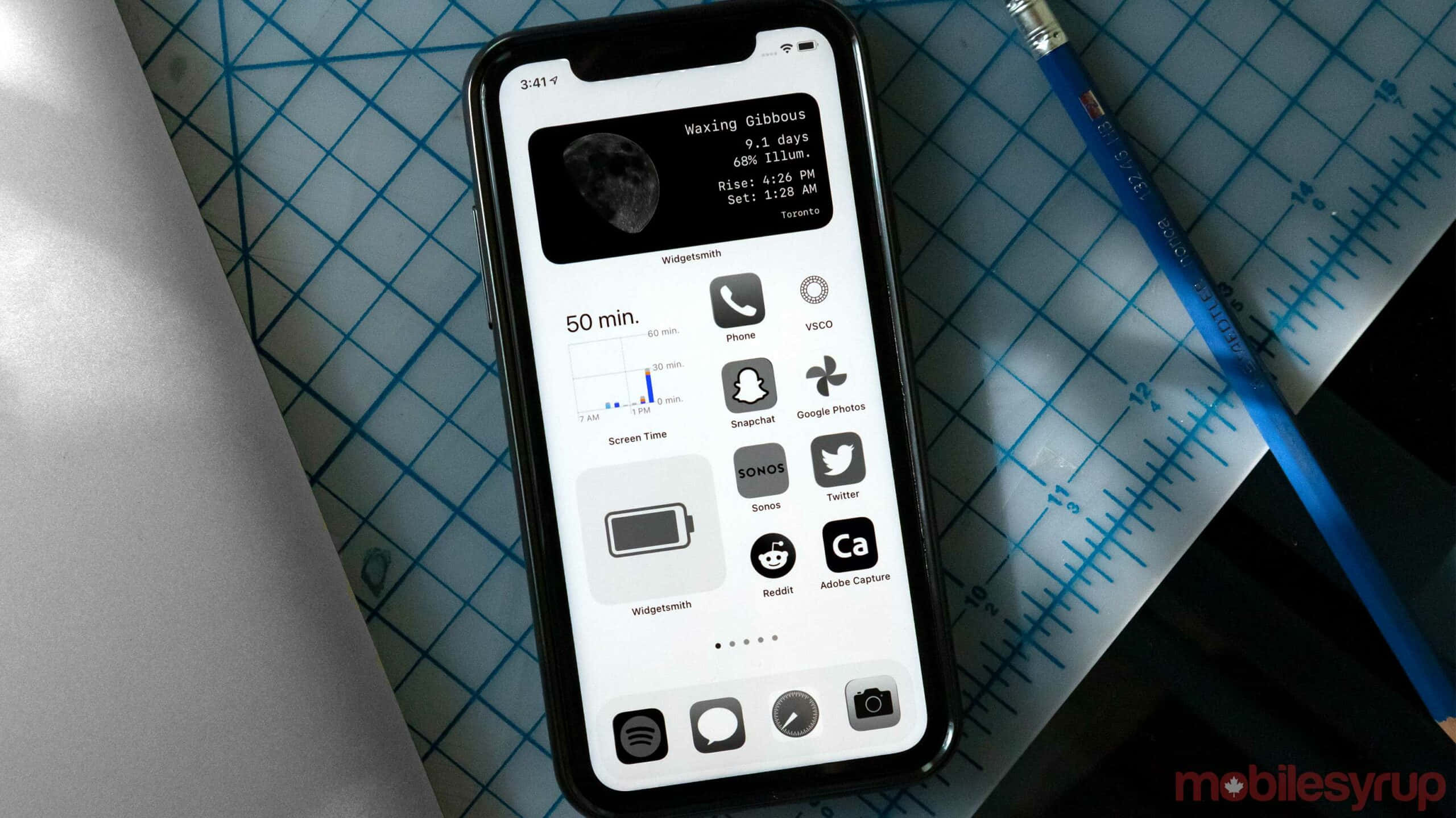 iPhone 美學 桌布 壁紙 — 一部顯示月相小工具和應用程式圖示的智慧型手機，放在藍色網格切割墊上，旁邊有一支藍色鉛筆。