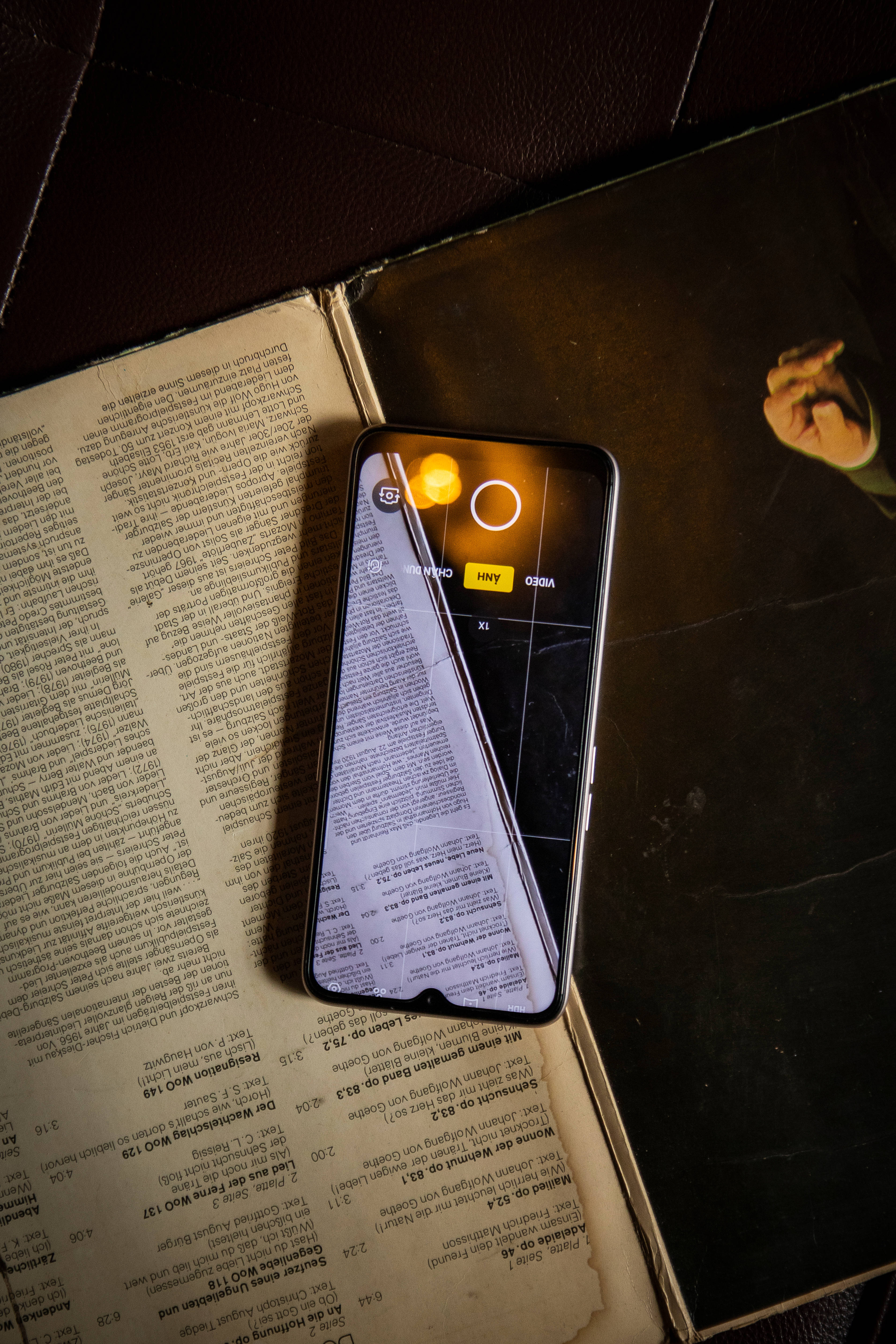 oppo 桌布 壁紙 — 一部顯示相機應用程式的智慧型手機放在一本打開的書本上，書本有文字，處於溫暖的環境燈光下。