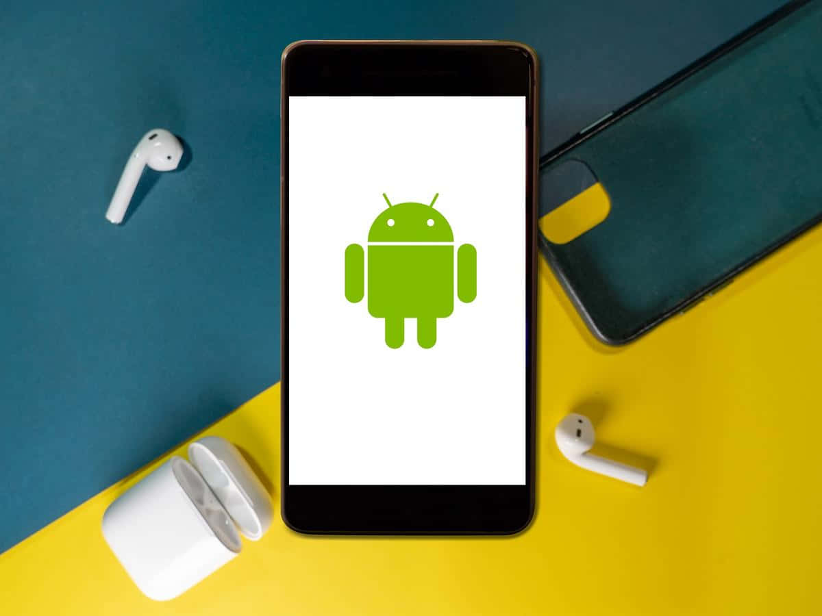 安卓 桌布 壁紙 — 一部顯示綠色Android機器人標誌的智慧型手機放在鮮黃色和藍綠色的表面上，附近有白色無線耳機。