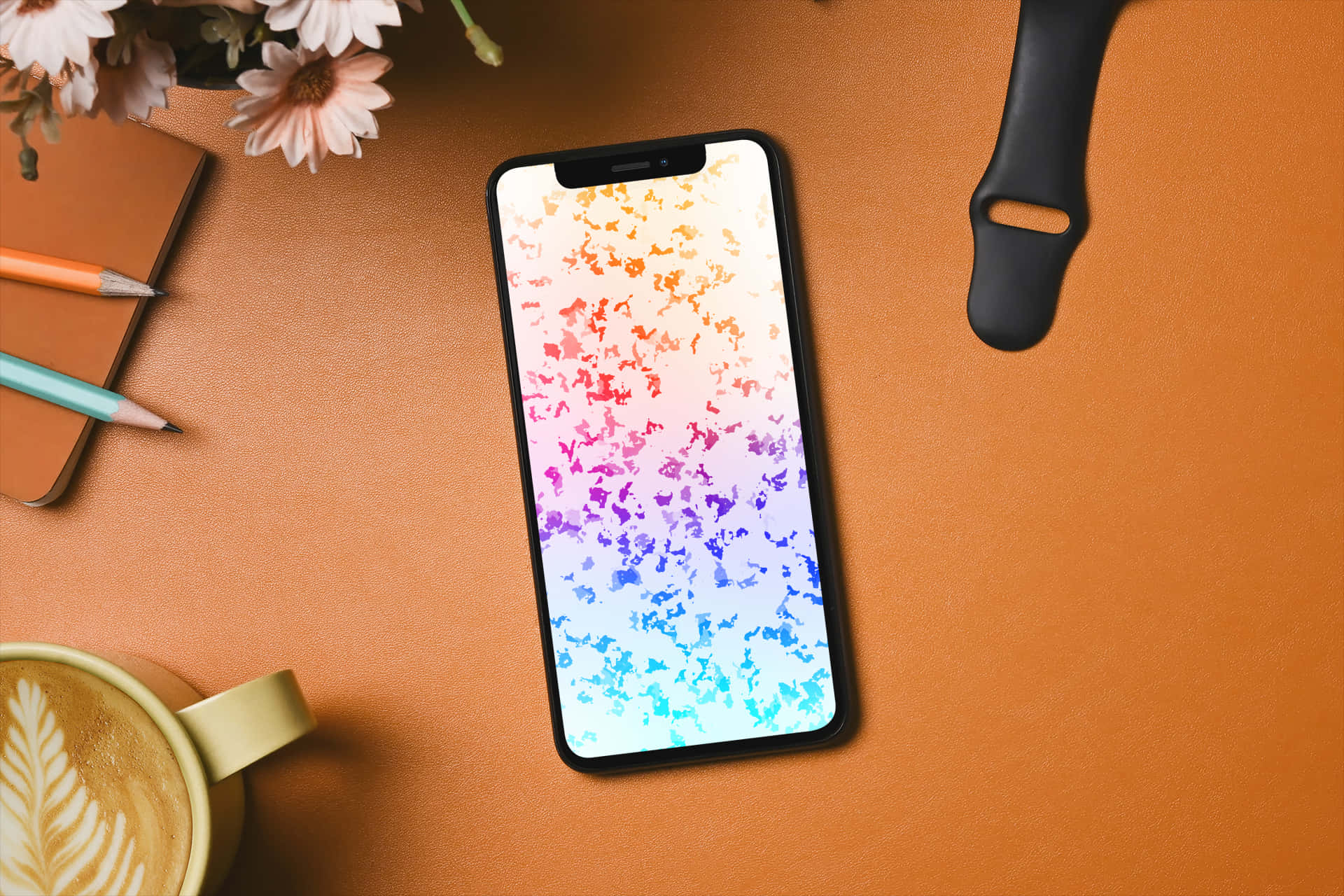Phone Screen 桌布 壁紙 — 一部顯示色彩繽紛抽象桌布的智慧型手機，放在溫暖的橙色桌子上，旁邊有拿鐵、鉛筆和花朵。