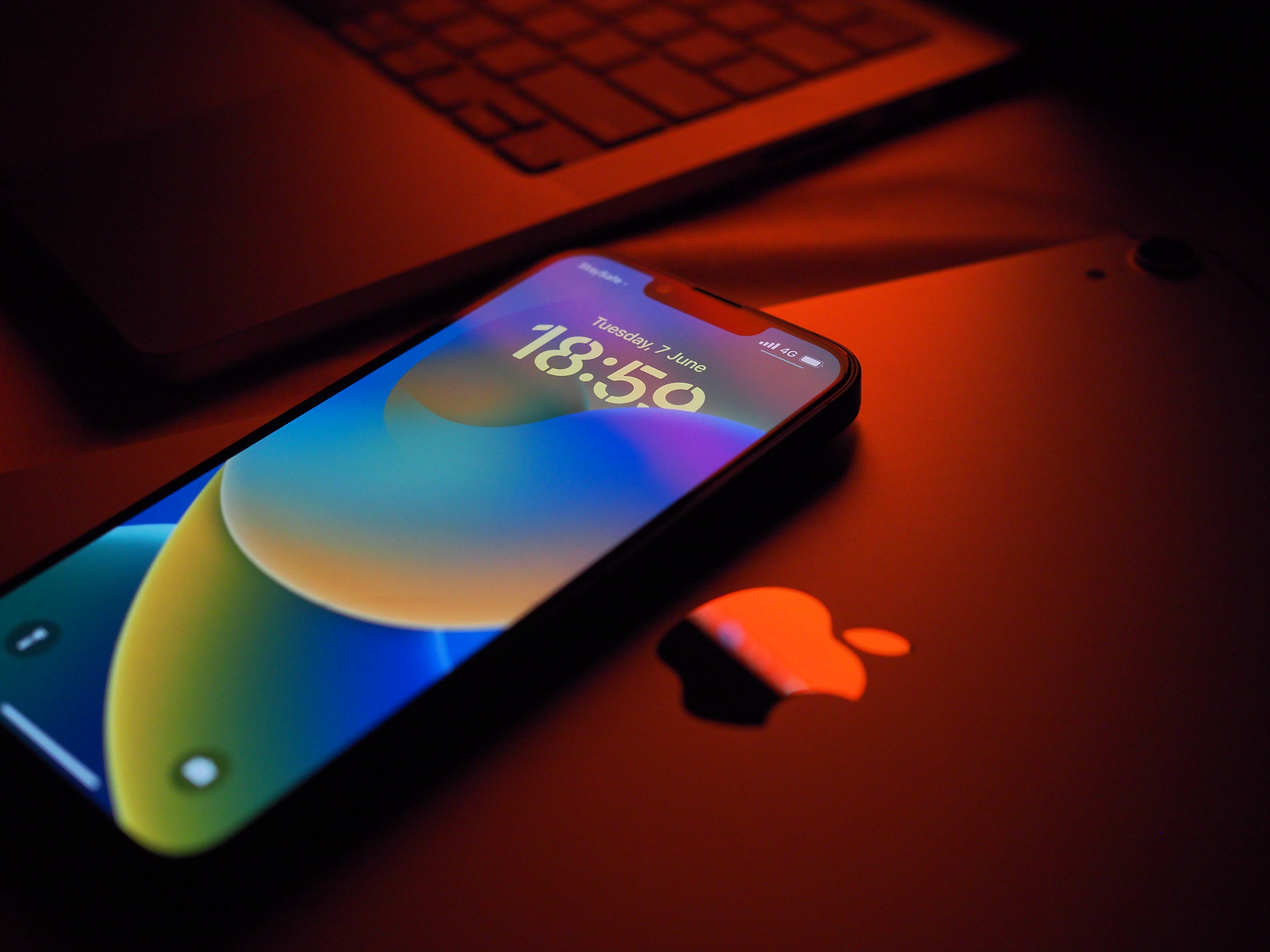 iOS 16 壁紙 桌布 壁紙 — 一部顯示鮮豔漸層桌布的智慧型手機，在溫暖的環境光線下放在筆記型電腦上。