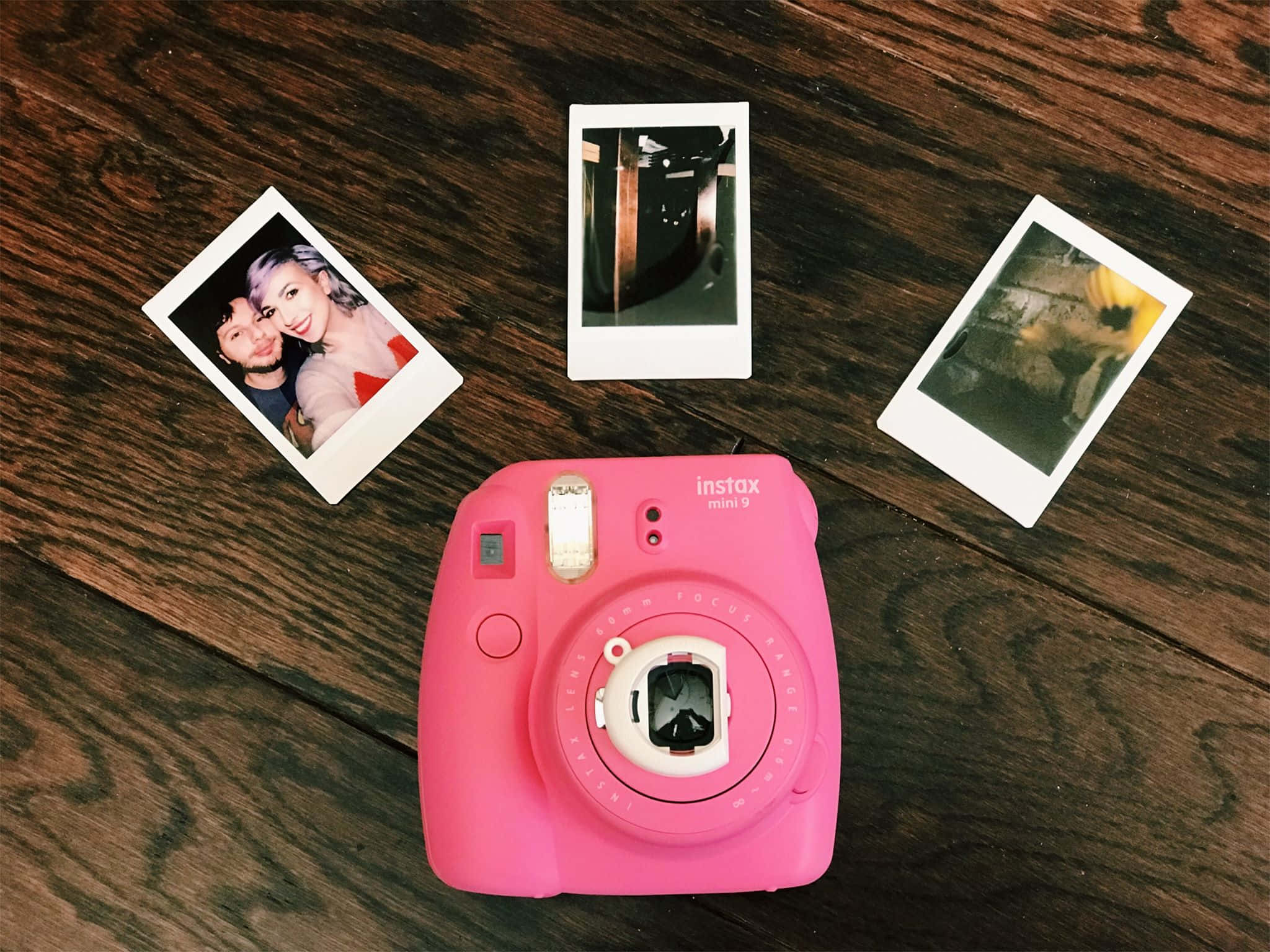 Photograph 桌布 壁紙 — 一部鮮粉紅色的Instax Mini 9相機放在深色木質表面上，周圍有三張即時照片。