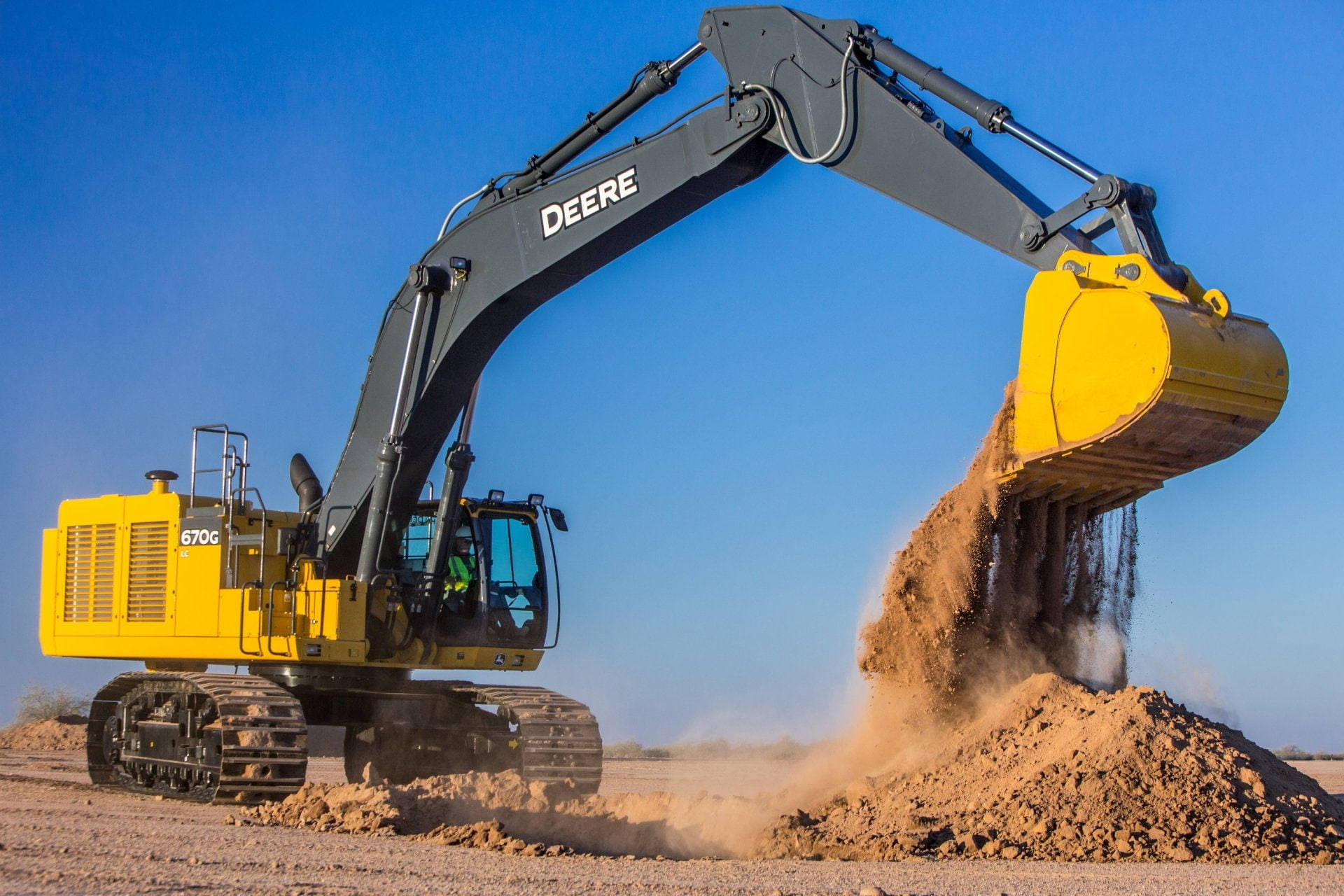 約翰迪爾 桌布 壁紙 — 一部黃色Deere 670G挖土機在晴朗藍天下於塵土飛揚的沙漠中傾倒泥土。