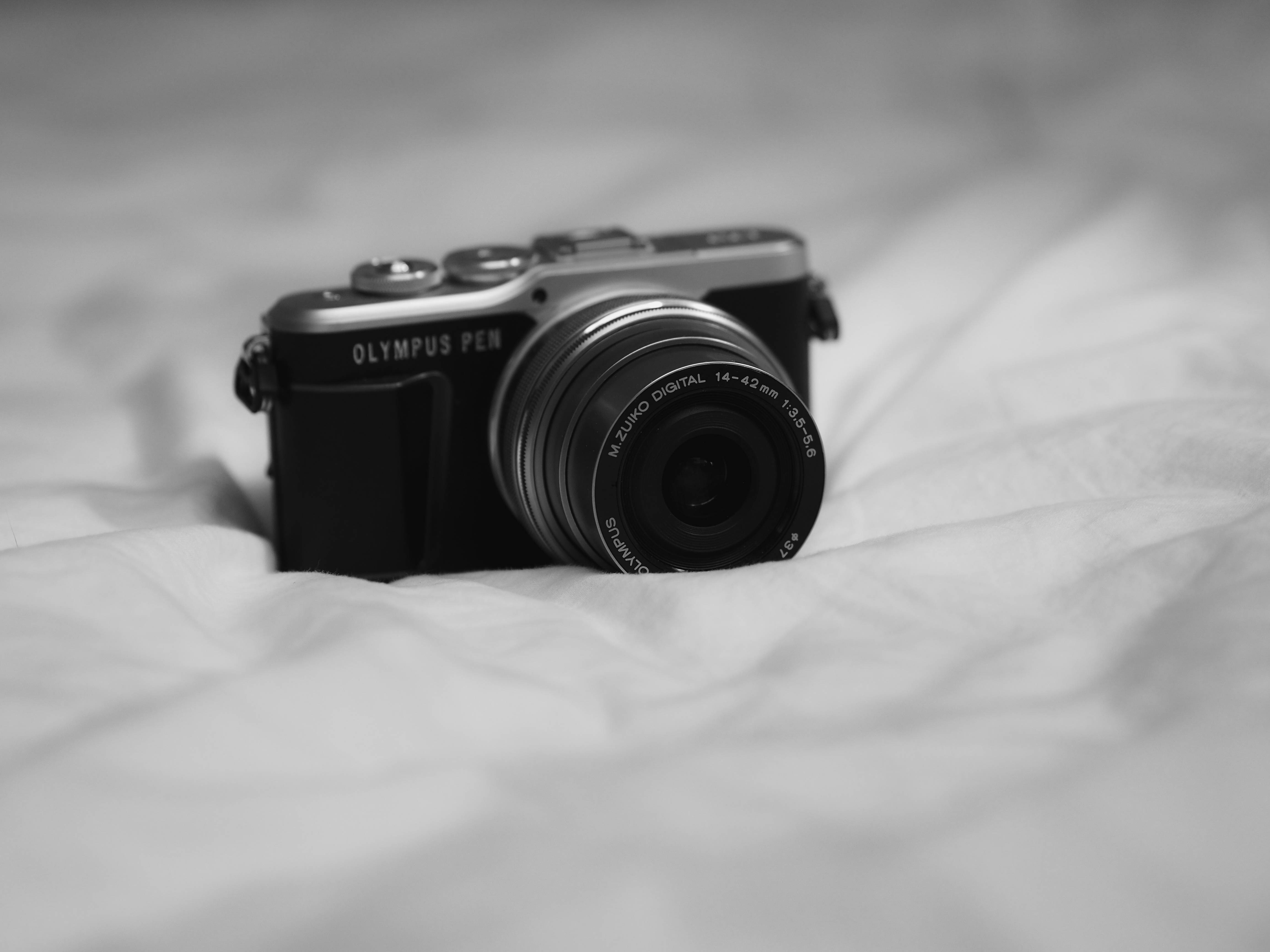 黑白美學動圖 桌布 壁紙 — 一部黑白 Olympus Pen 相機放在皺褶的布料上，背景柔和模糊。