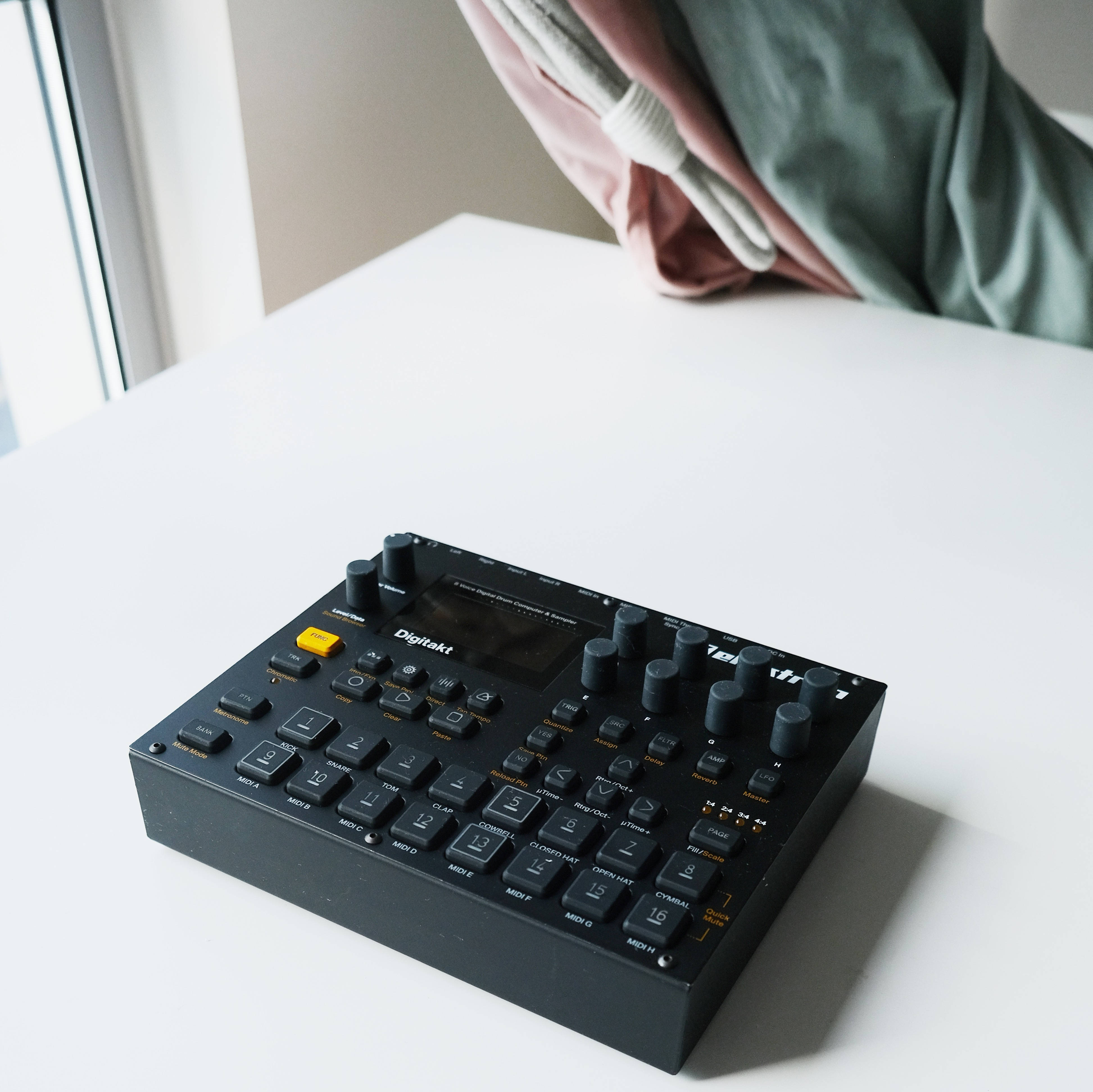 低傳真 桌布 壁紙 — 一部黑色 Digitakt 音樂序列器放在白色桌子上，靠近窗戶，光線柔和自然，背景有粉綠色布料垂掛。
