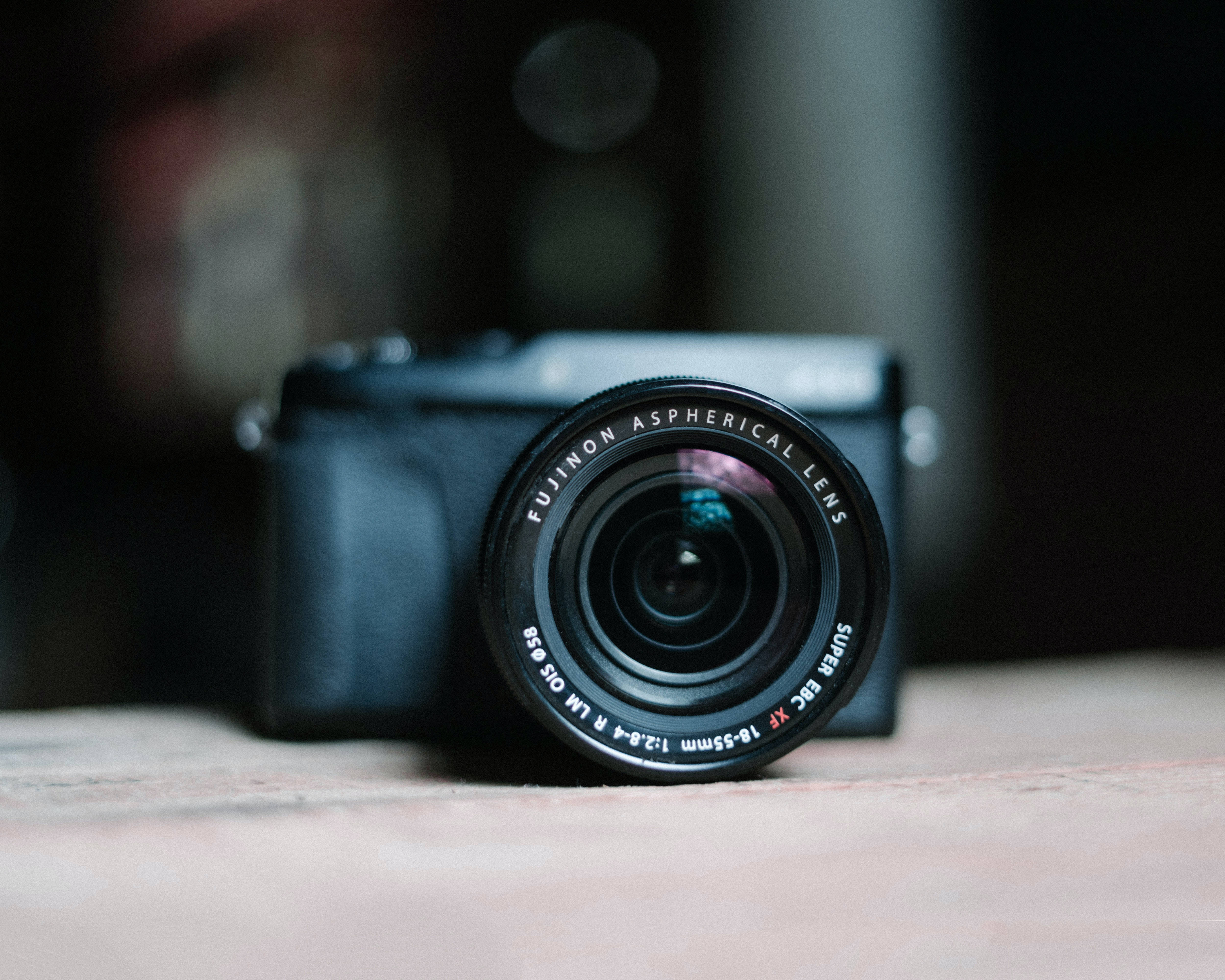 相機 桌布 壁紙 — 一部黑色 Fujifilm 相機配備 Fujinon 鏡頭，放置在木質表面上，具有淺景深和柔和背景散景。