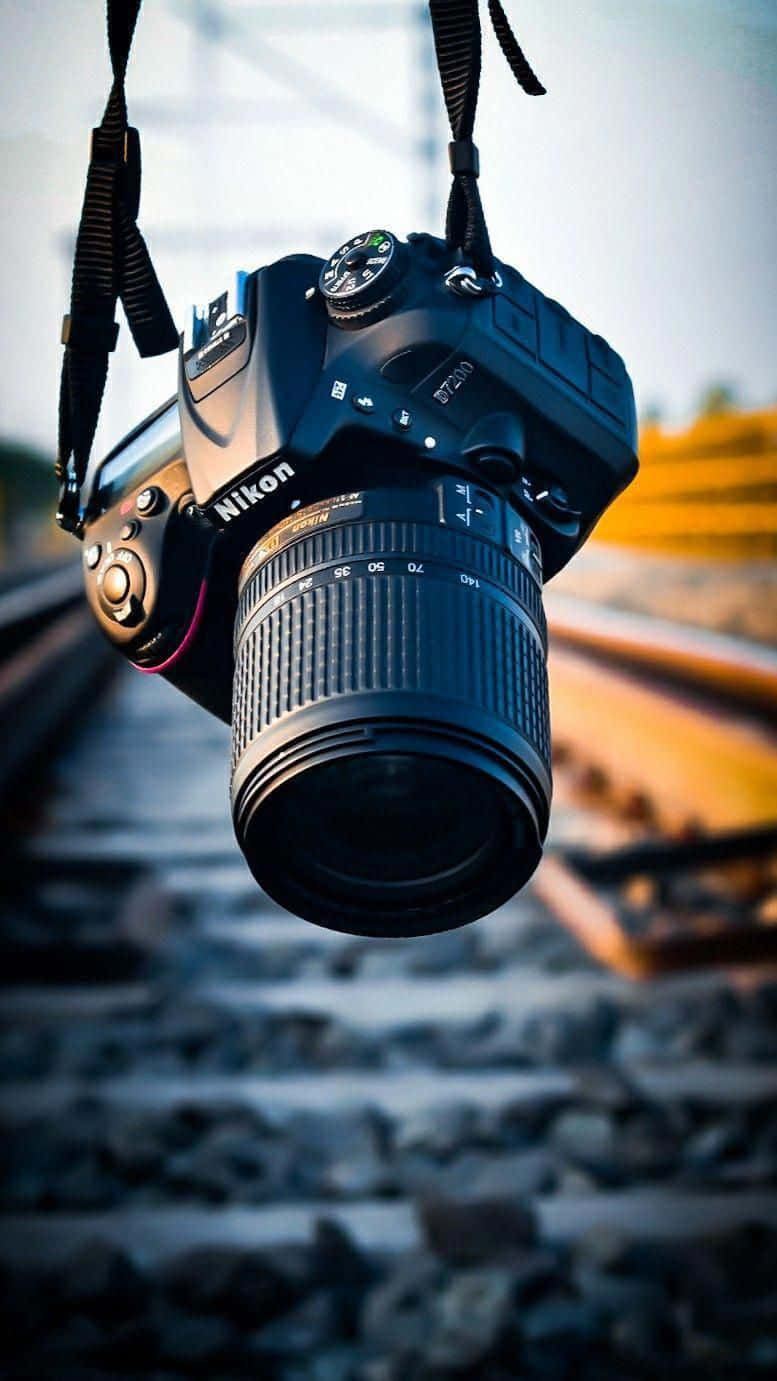 攝影 桌布 壁紙 — 一部黑色 Nikon DSLR 相機用帶子懸掛在模糊的鐵路軌道上，在柔和日光下。