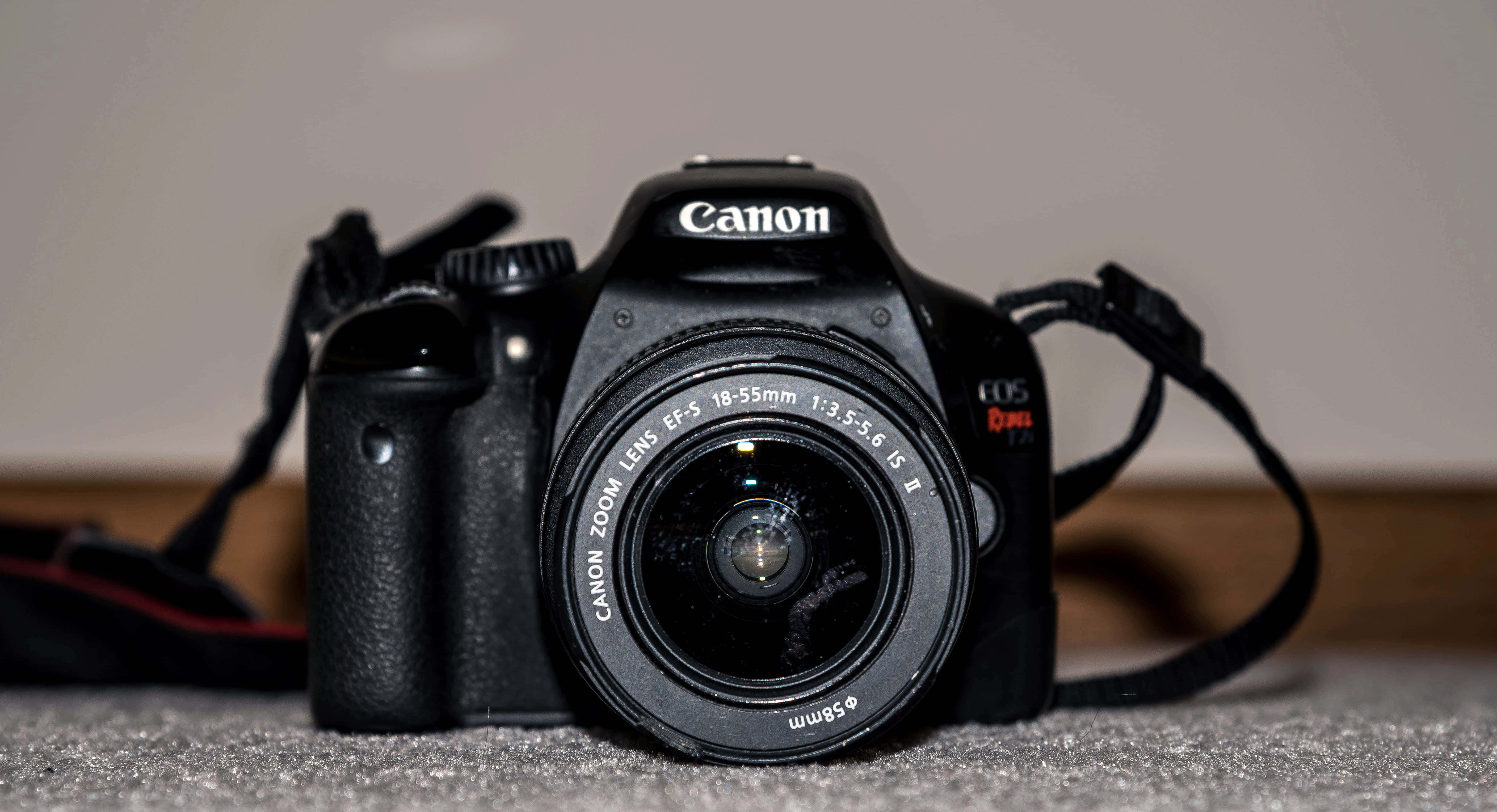 相機 桌布 壁紙 — 一部黑色Canon DSLR相機配備18-55mm鏡頭，放置在紋理灰色表面上，背景是柔和的米色牆壁。
