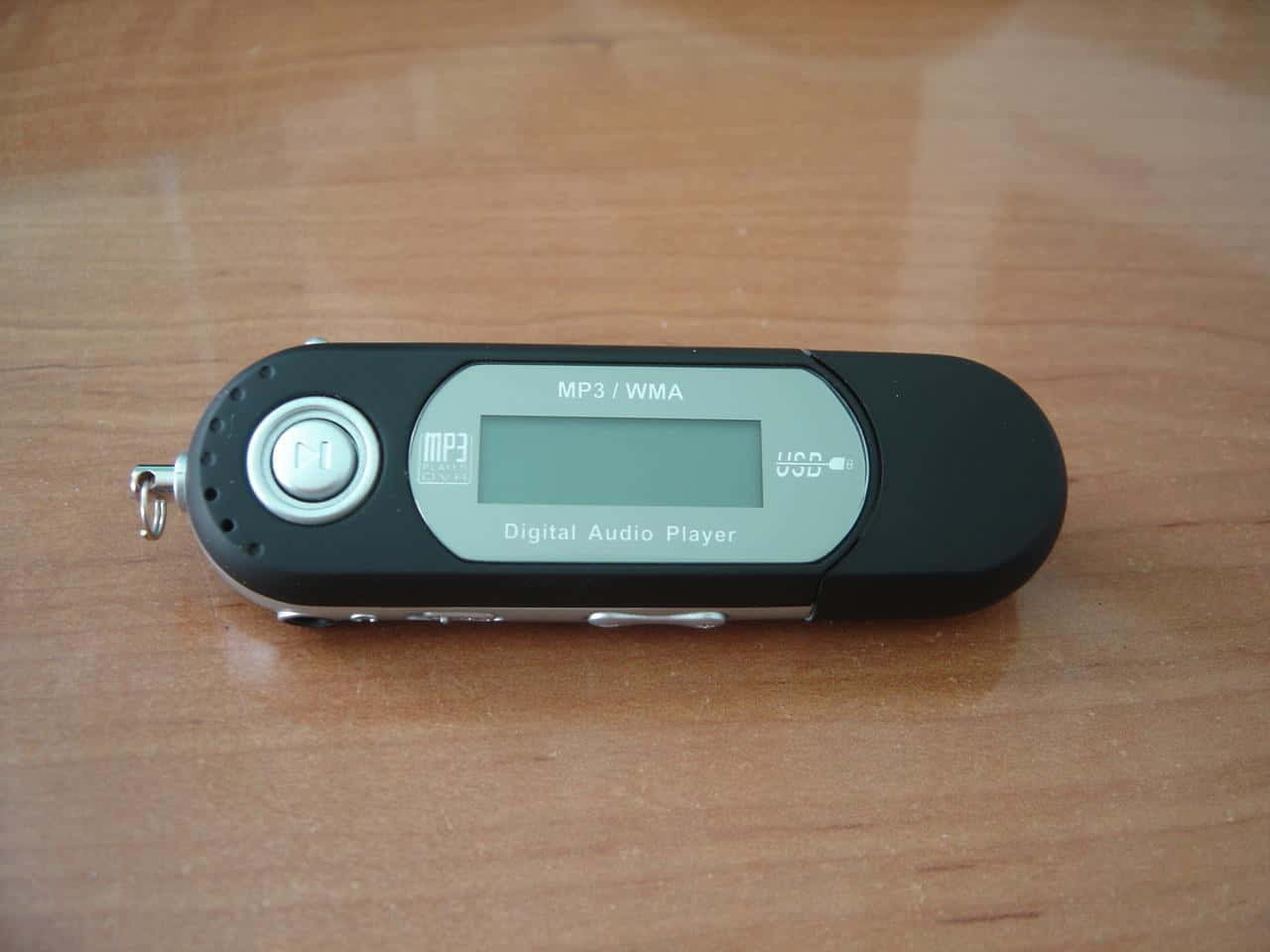 Music Player 桌布 壁紙 — 一部黑色數位音訊播放器帶有銀色點綴，放置在溫暖的木質表面上。