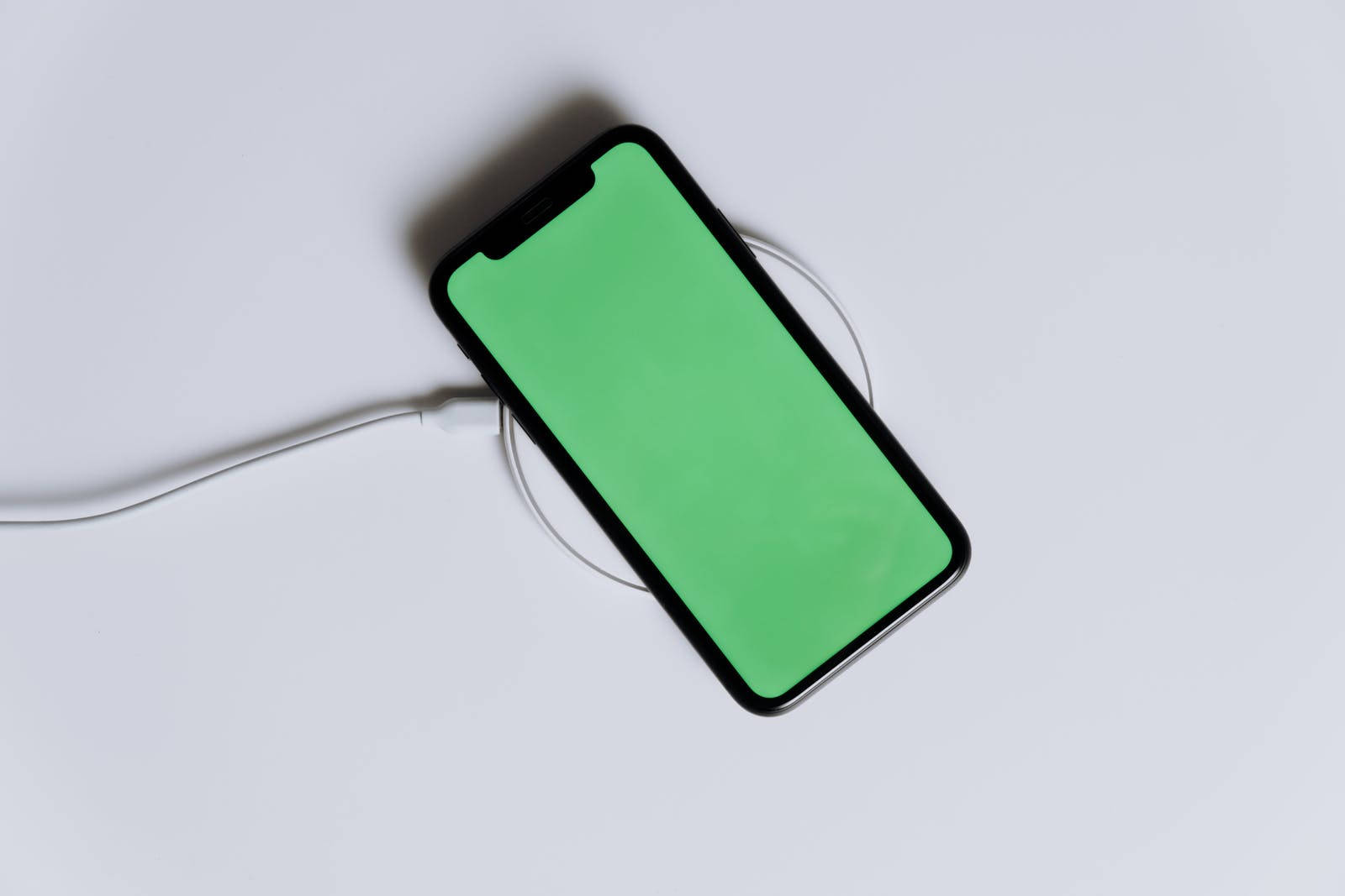 黑色智慧型手機在白色無線充電板上充電，綠色螢幕
