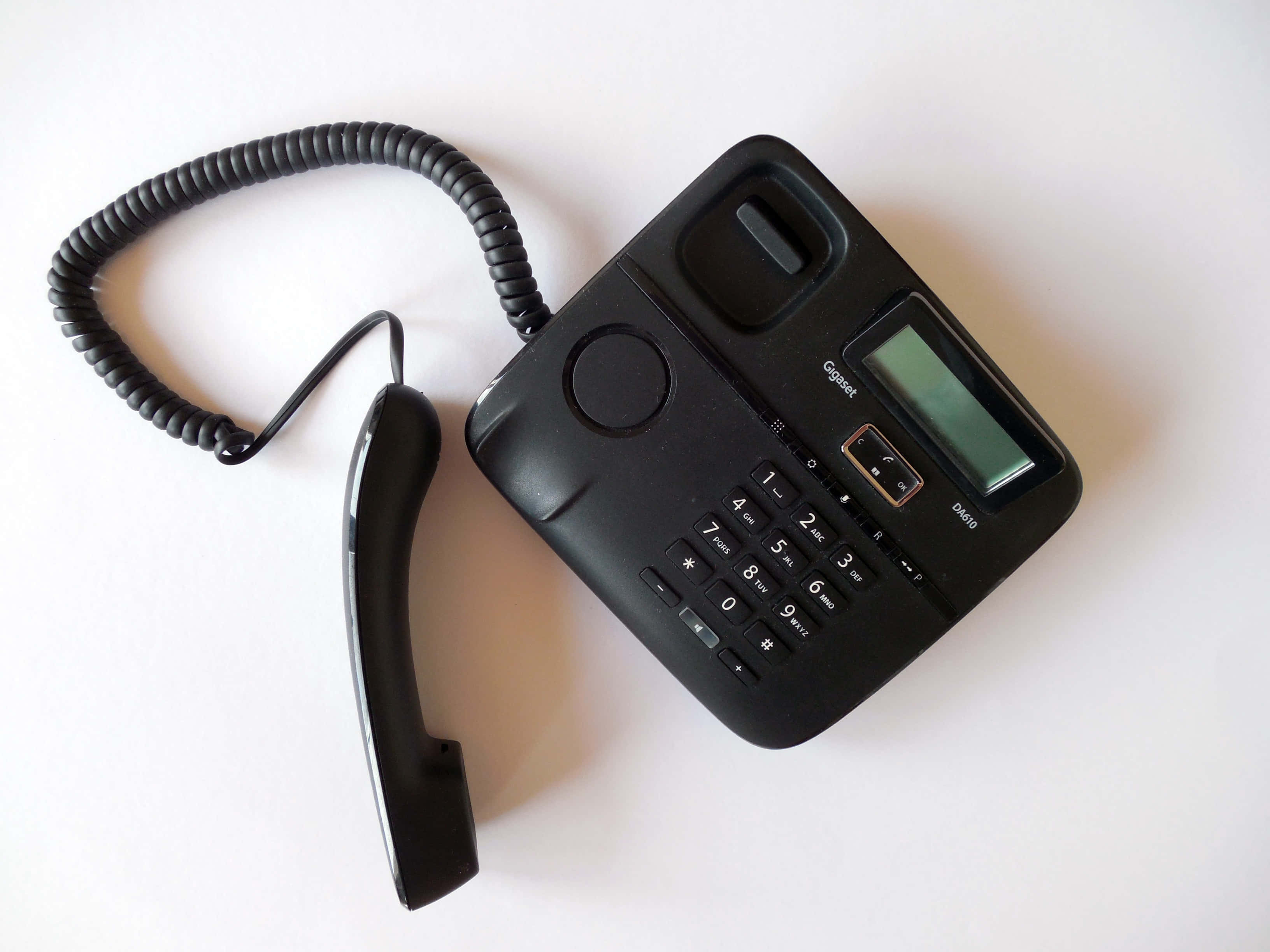 Phone Call 桌布 壁紙 — 一部黑色有線電話連聽筒放置在純白色表面上，展示其鍵盤和小螢幕。