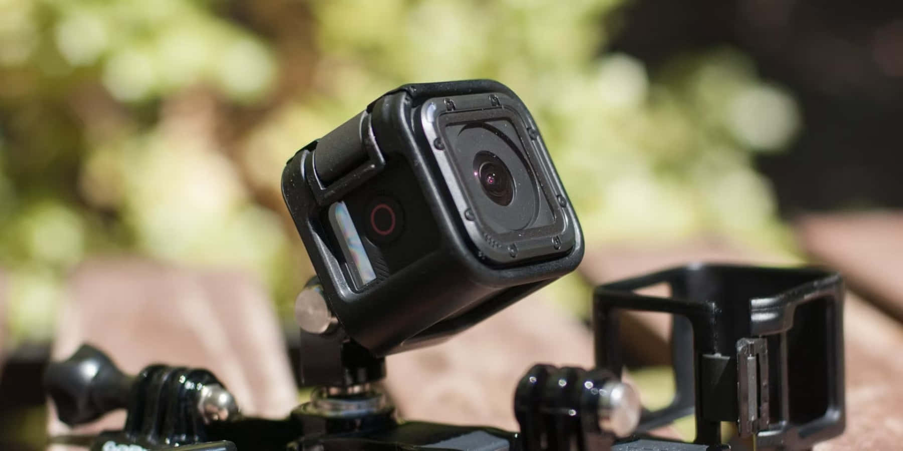 gopro 桌布 壁紙 — 一部黑色運動攝影機安裝在三腳架上，背景有模糊的綠色樹葉。