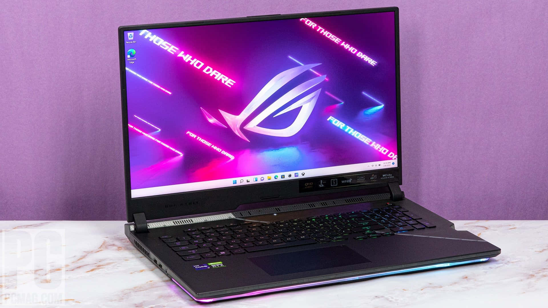 華碩 ROG 桌布 壁紙 — 一部黑色電競筆記型電腦帶有發光RGB裝飾，打開放在大理石表面上，對著紫色牆壁顯示充滿活力的霓虹桌布。