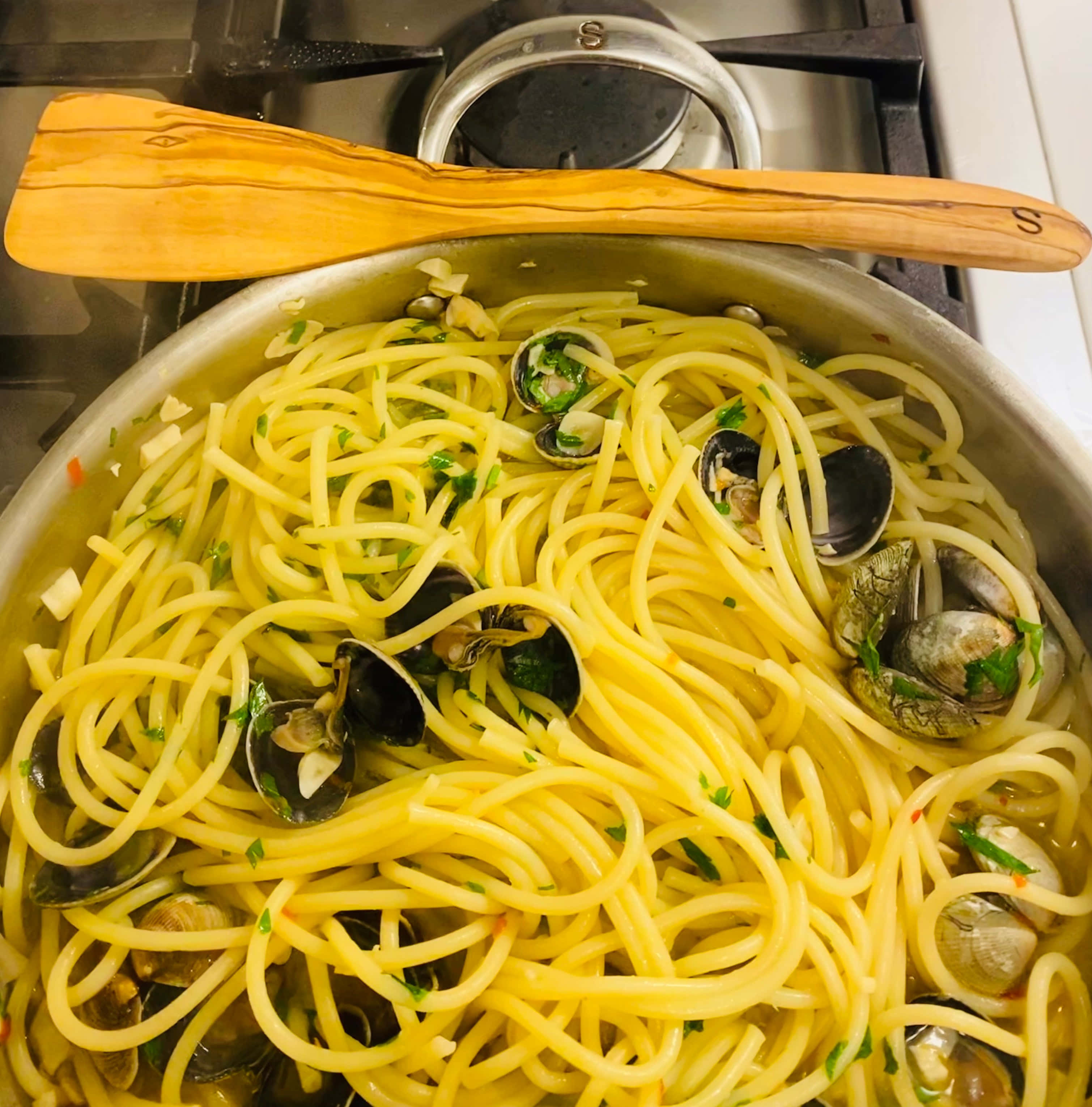 Clam 桌布 壁紙 — 一鍋冒著蒸氣的蛤蜊香草義大利麵放在爐灶上，邊緣擱著一隻木勺。