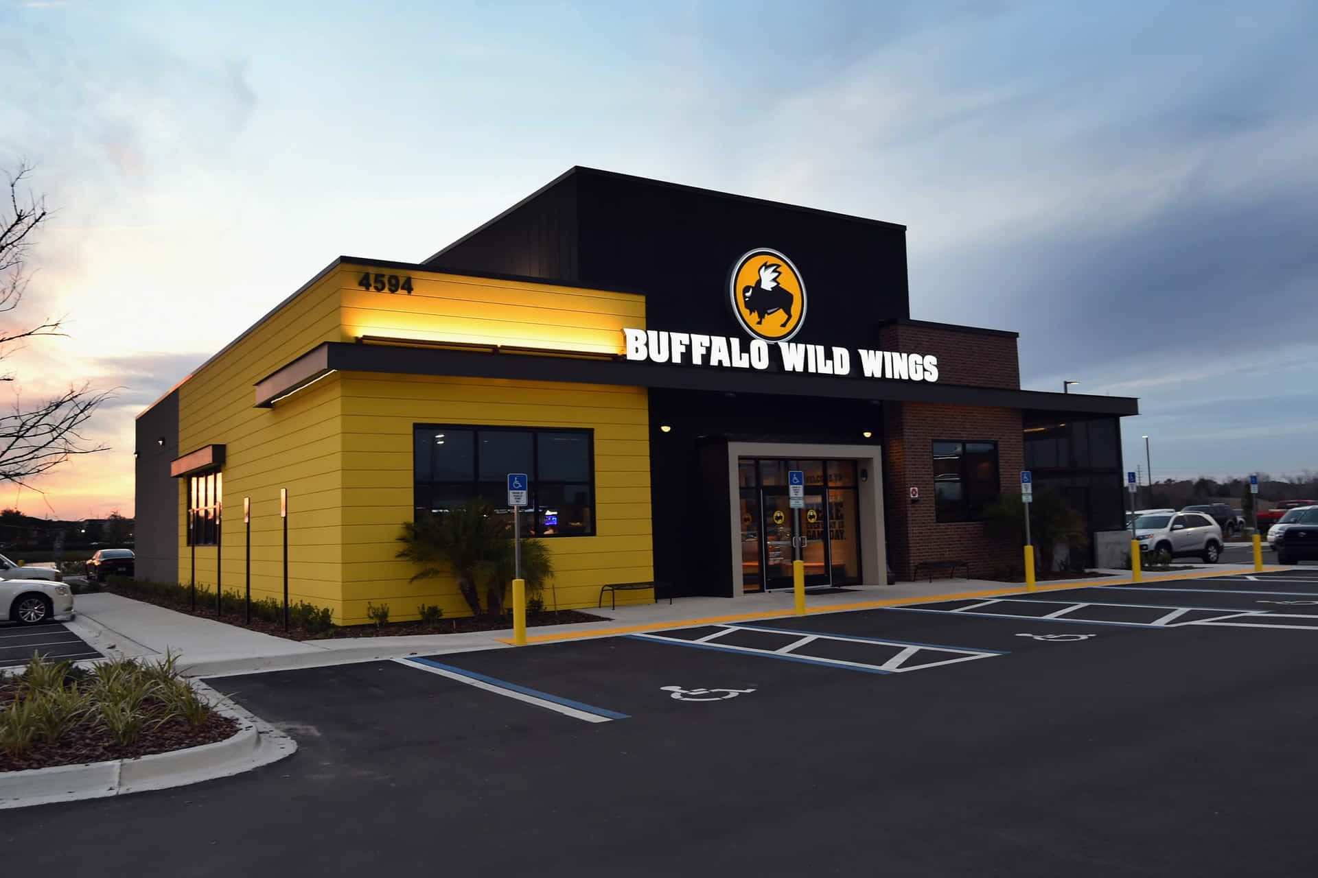 水牛城辣雞翅 桌布 壁紙 — 一間 Buffalo Wild Wings 餐廳在黃昏時分，鮮黃色牆壁和發光招牌在陰天天空下。