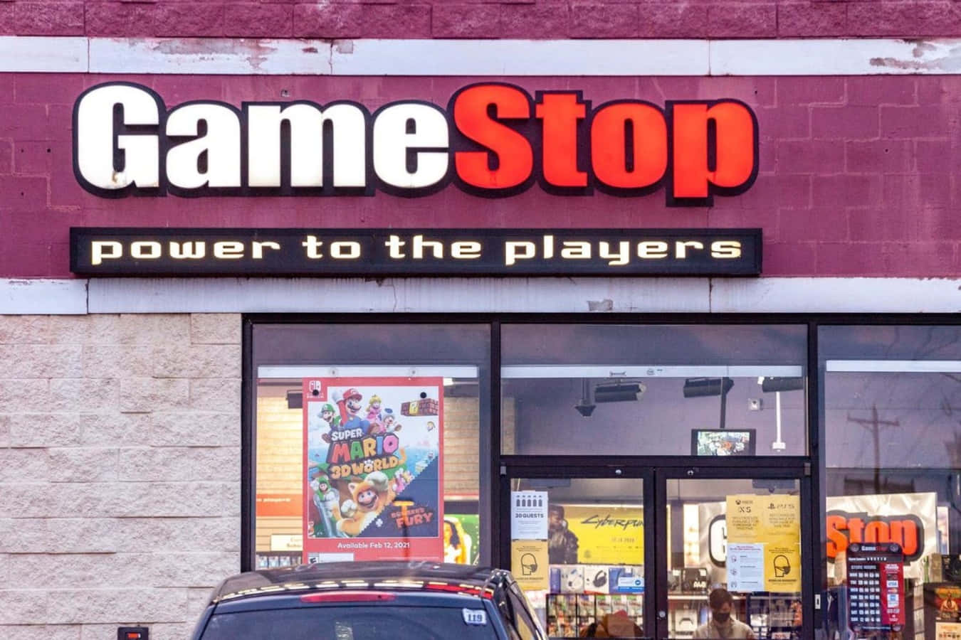 GameStop 桌布 壁紙 — 一間 GameStop 店面外觀，帶有醒目的紅白招牌，窗戶上可見 Super Mario 3D World 海報。