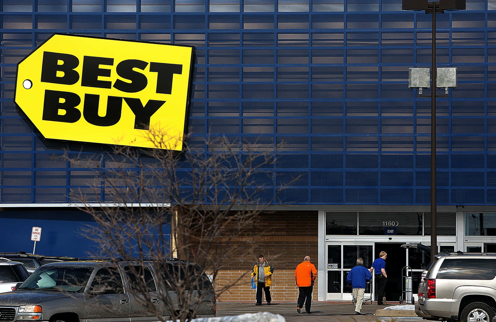 Best Buy 桌布 壁紙 — 一間Best Buy商店，藍色外牆和黃色標誌，購物者進入，汽車在附近停車。