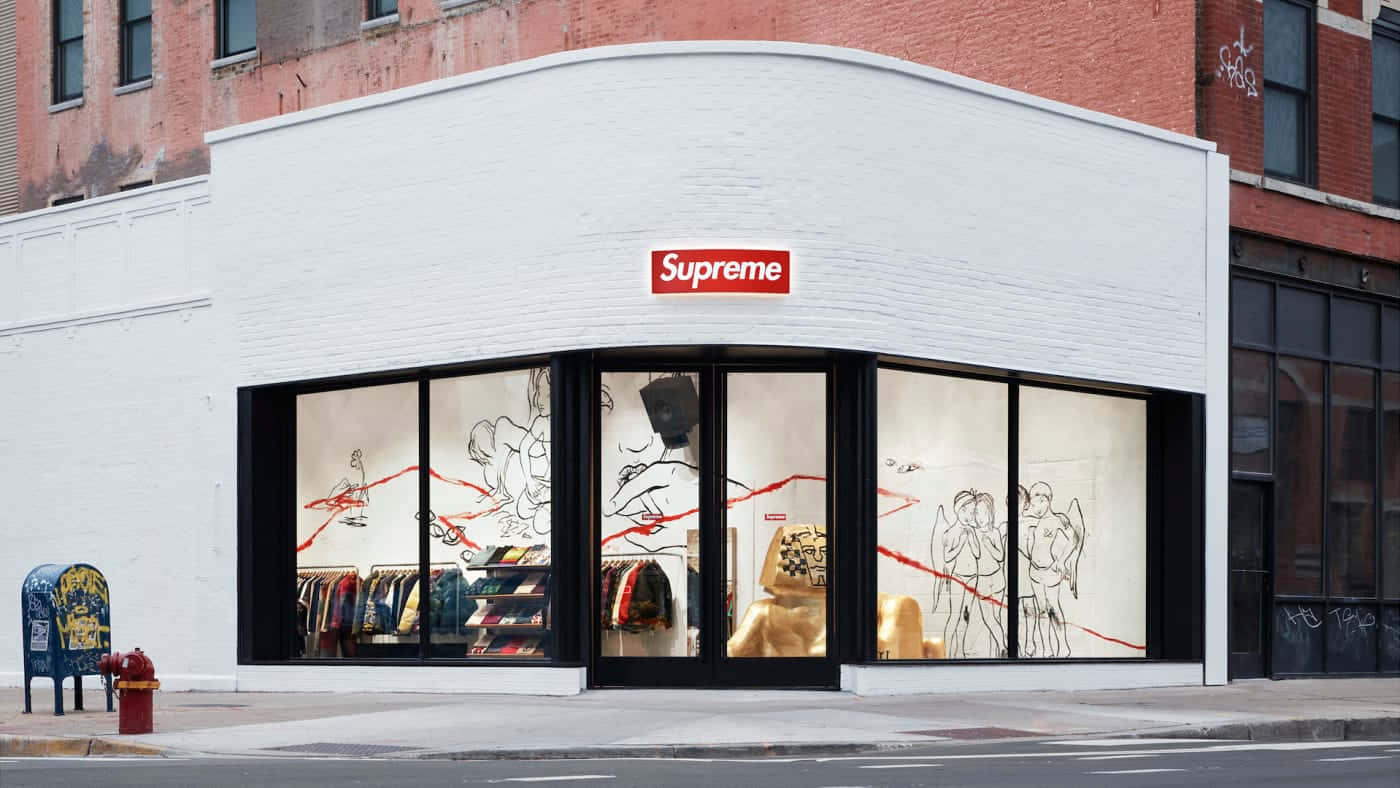 supreme 桌布 壁紙 — 一間Supreme角落店舖，帶有醒目的紅色標誌、白色磚牆外牆和展示街頭服飾草圖及貨架的大窗戶。