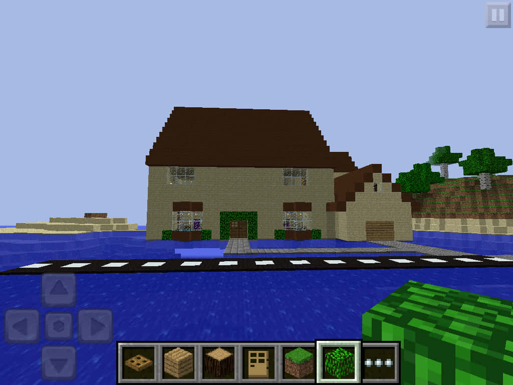Minecraft Pocket Edition 桌布 壁紙 — 一間像素風格的Minecraft房屋，棕色屋頂和綠色邊飾，矗立在藍色水邊的鵝卵石小徑上，天空晴朗。