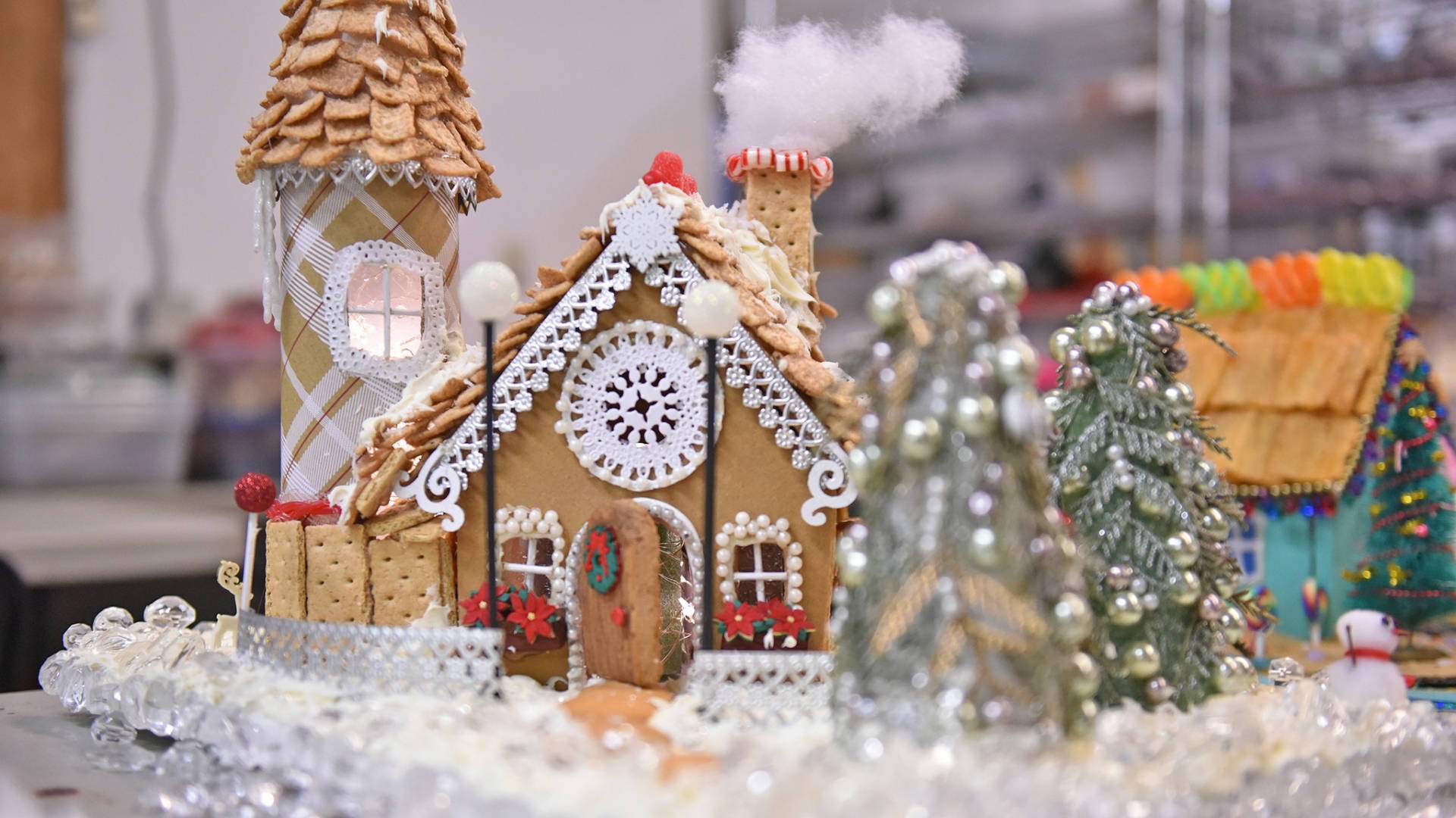 Gingerbread House 桌布 壁紙 — 一間充滿奇思妙想的薑餅屋，飾有糖蕾絲和餅乾瓦片，坐落在閃閃發光的糖果樹旁，在雪景中展示。