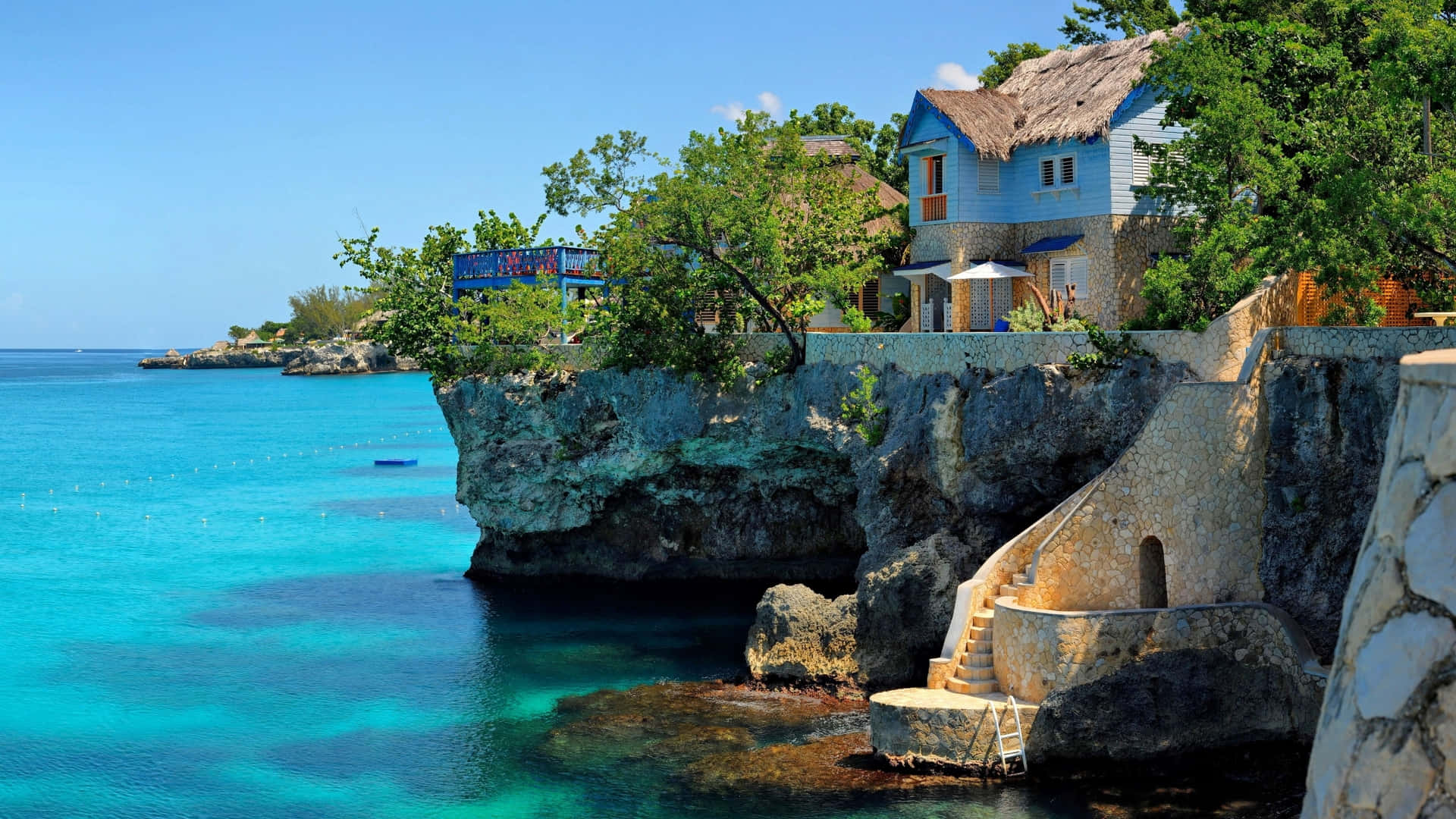 Jamaica 桌布 壁紙 — 一間充滿活力的藍色房屋坐落在岩石懸崖上，俯瞰著明亮藍天下清澈的碧綠海水。