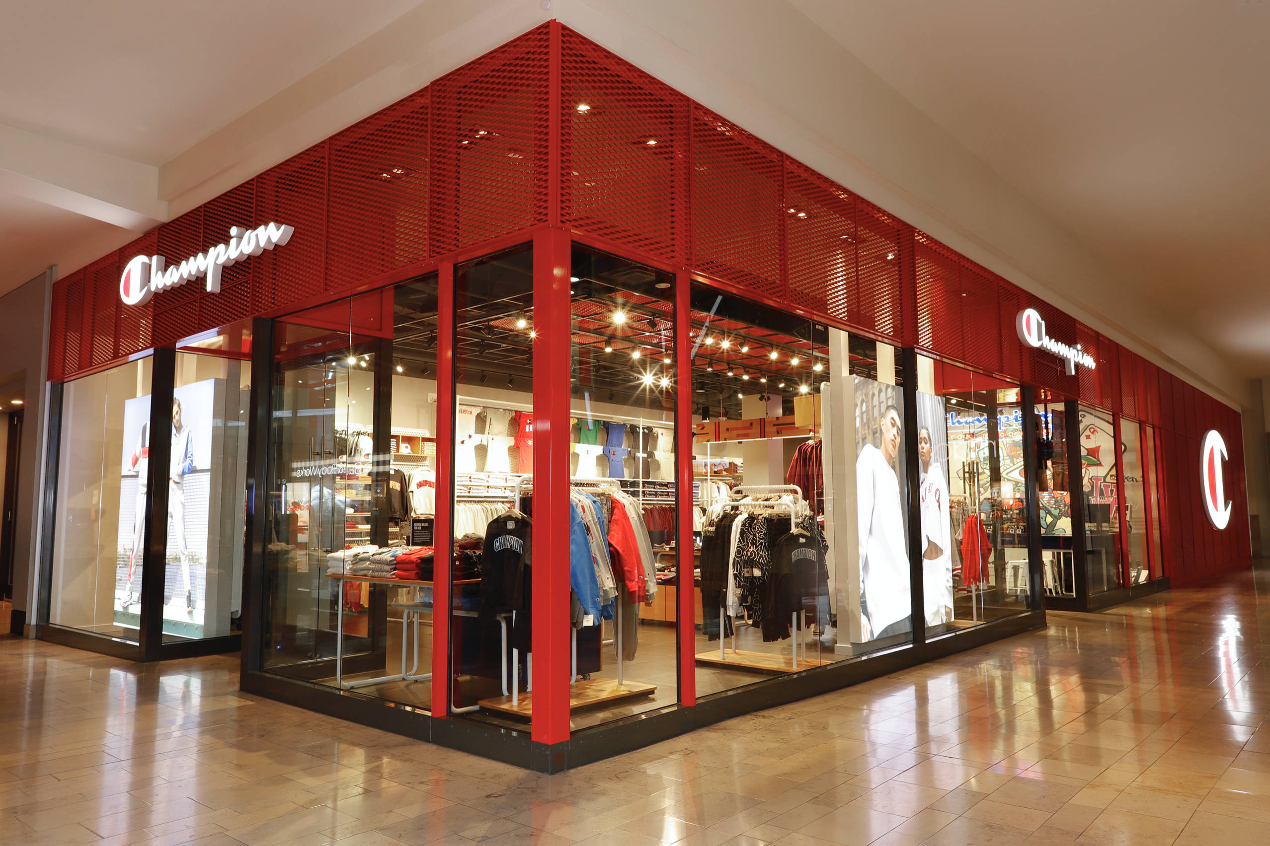 Champion 桌布 壁紙 — 一間光線充足的Champion運動服飾店，配有紅色金屬面板和玻璃窗，在購物中心內展示運動服裝。