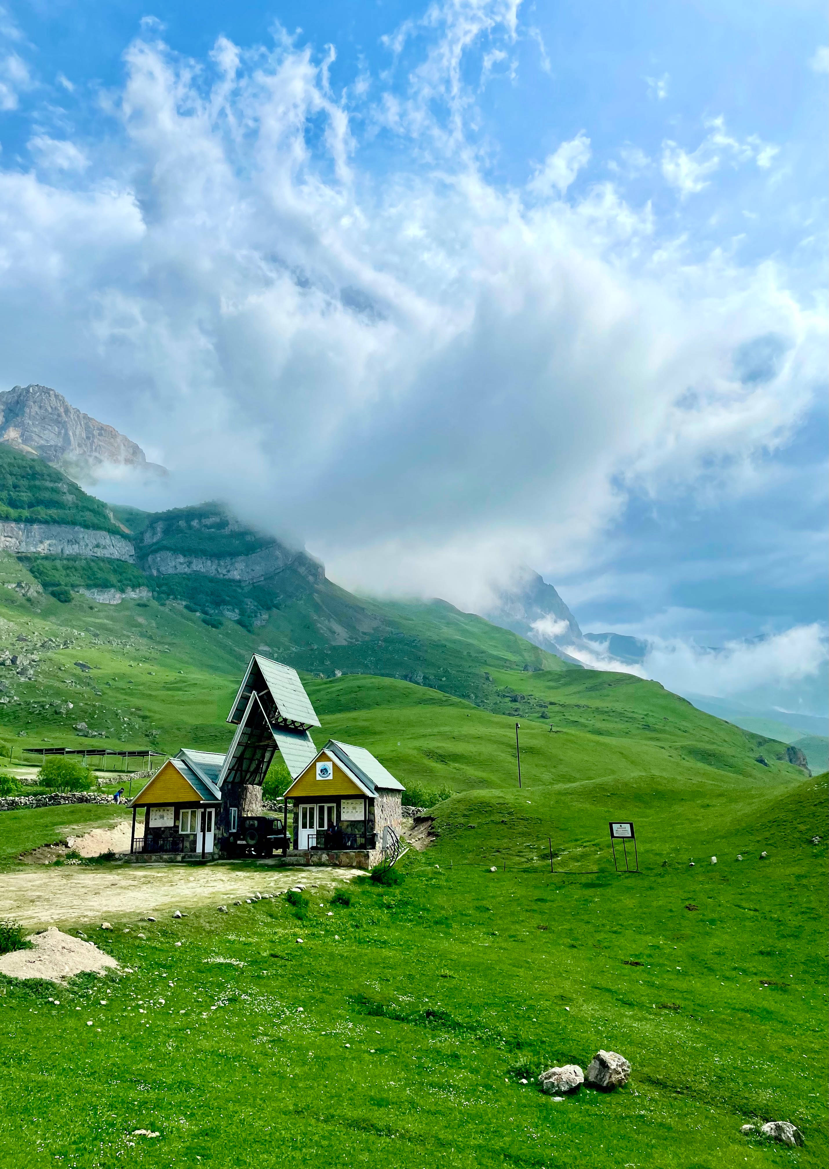Azerbaijan 桌布 壁紙 — 一間古雅的黃色山間小屋，坐落在鬱鬱蔥蔥的綠色草地上，上方是戲劇性的多雲天空。