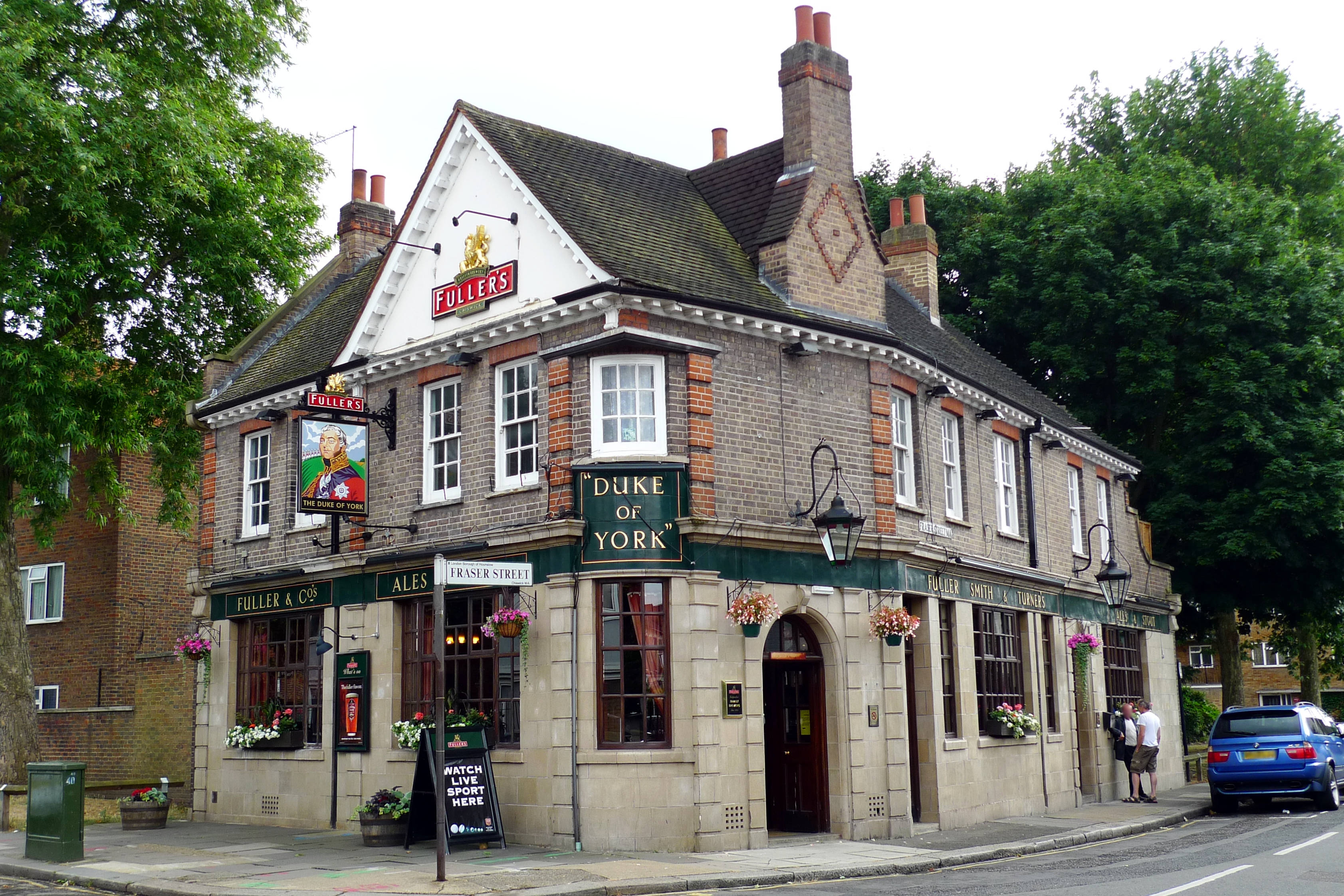 Pub 桌布 壁紙 — 一間名為 Duke of York 的傳統磚砌酒吧，門外掛有花籃，並有一輛藍色汽車停泊。