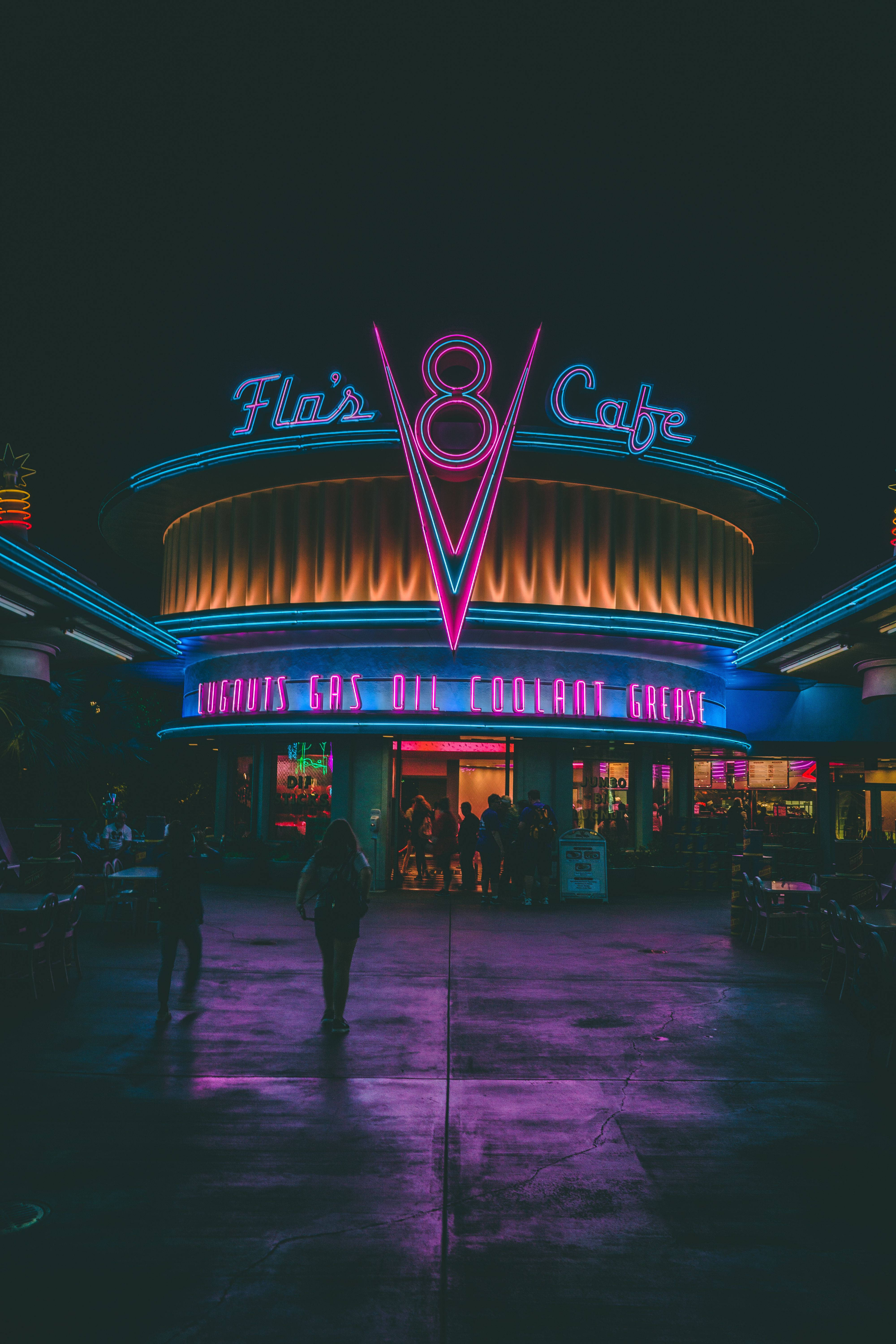 lights 桌布 壁紙 — 一間名為 Fla's V8 Cafe 的復古餐廳在漆黑的夜空下閃爍著鮮豔的霓虹燈牌，在濕漉漉的路面上投射出色彩繽紛的倒影，剪影人物走過。