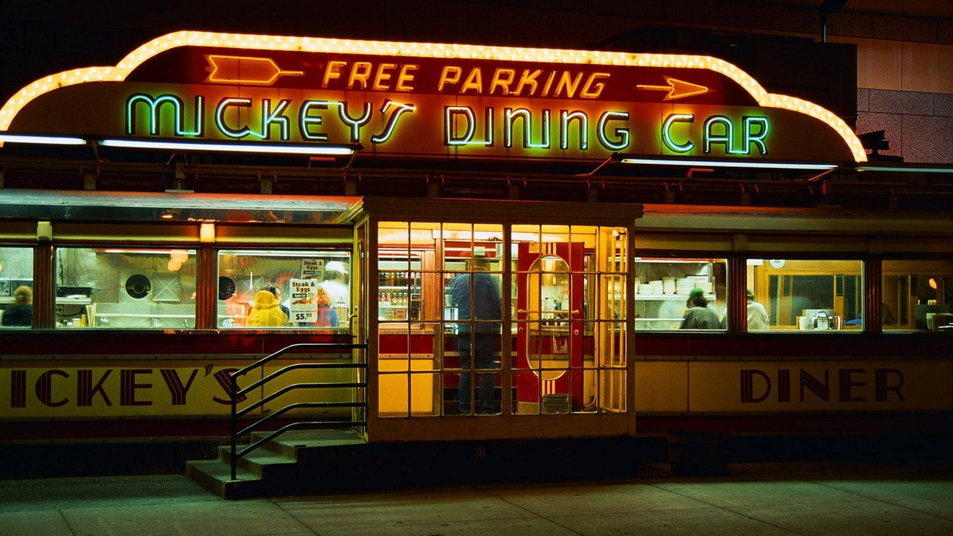 Diner 桌布 壁紙 — 一間名為 Mickey's Dining Car 的復古餐廳在夜晚閃爍著霓虹燈招牌，透過窗戶將溫暖的光線投射到人行道上。