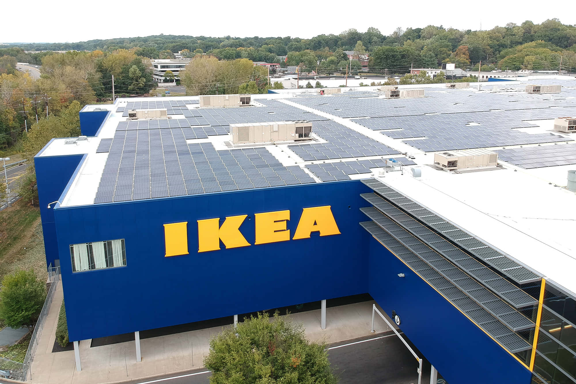 Ikea 桌布 壁紙 — 一間大型藍色IKEA商店的鳥瞰圖，屋頂覆蓋太陽能板，周圍樹木呈現秋色。