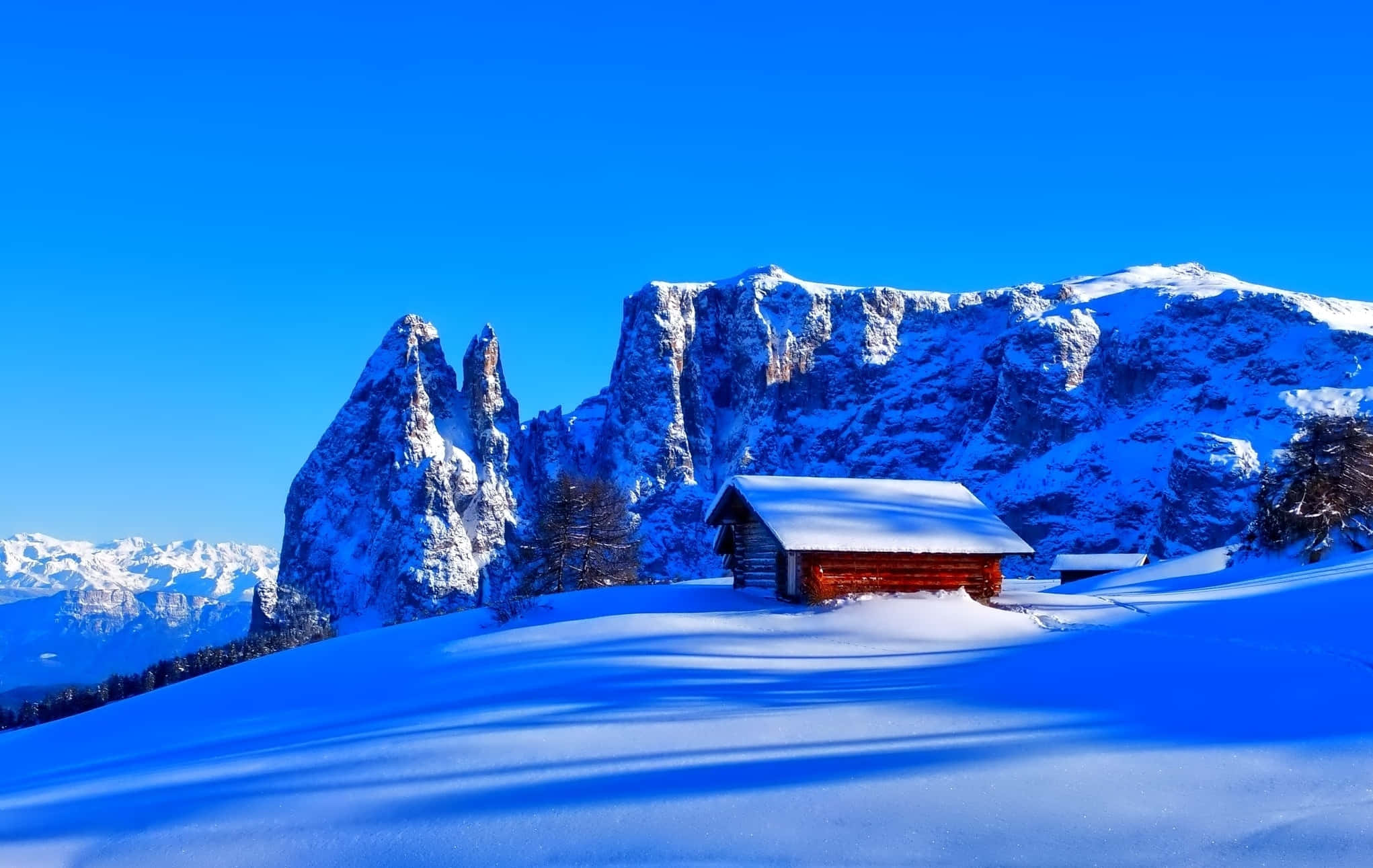 Hut 桌布 壁紙 — 一間孤獨的紅色小屋坐落在白雪覆蓋的山脈中，上方是鮮豔的藍天。