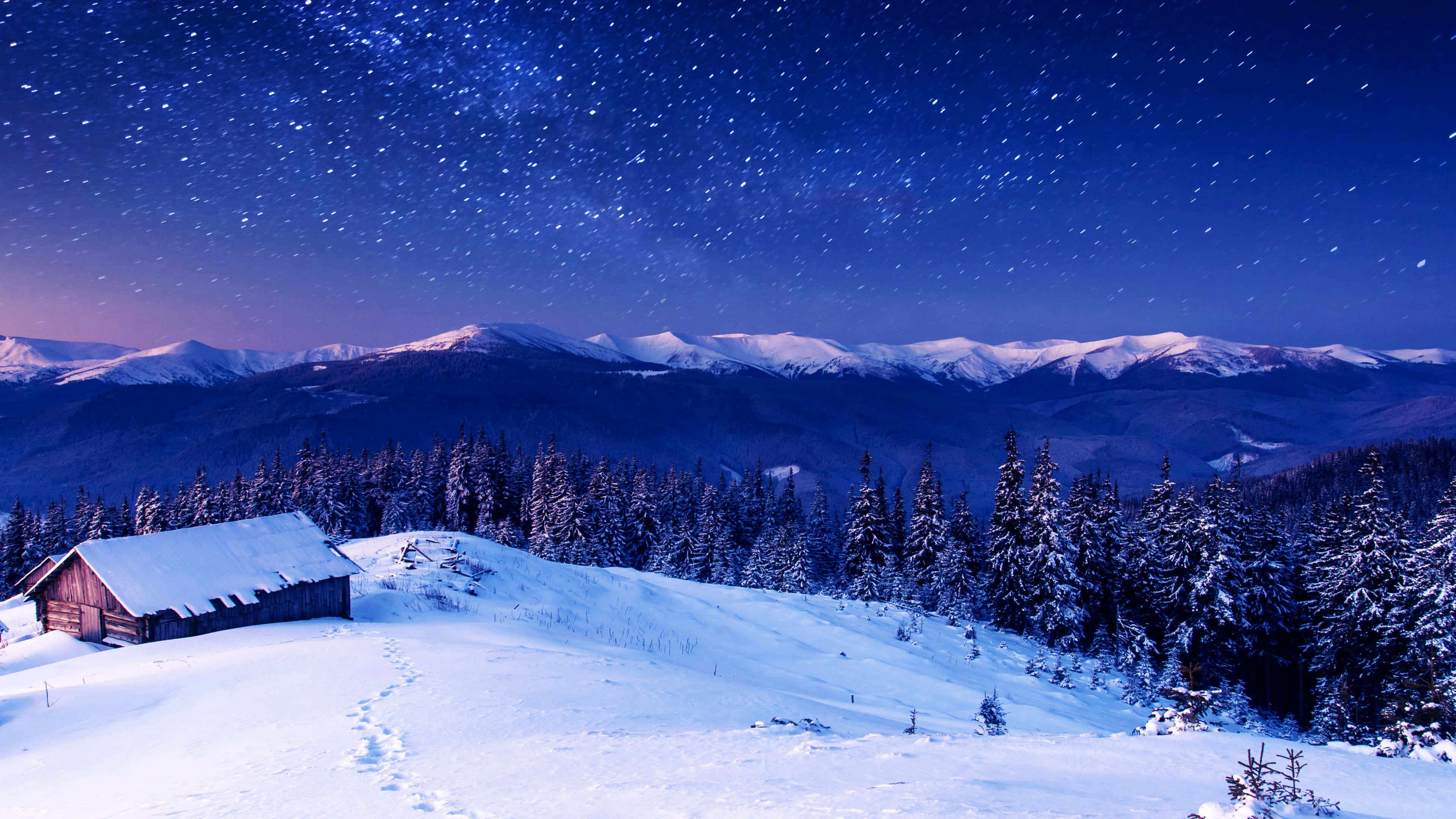 Ski Mountain 桌布 壁紙 — 一間孤獨的雪覆蓋的小屋坐落在冬季森林中，在繁星點點的夜空下，遠處有積雪的山峰。
