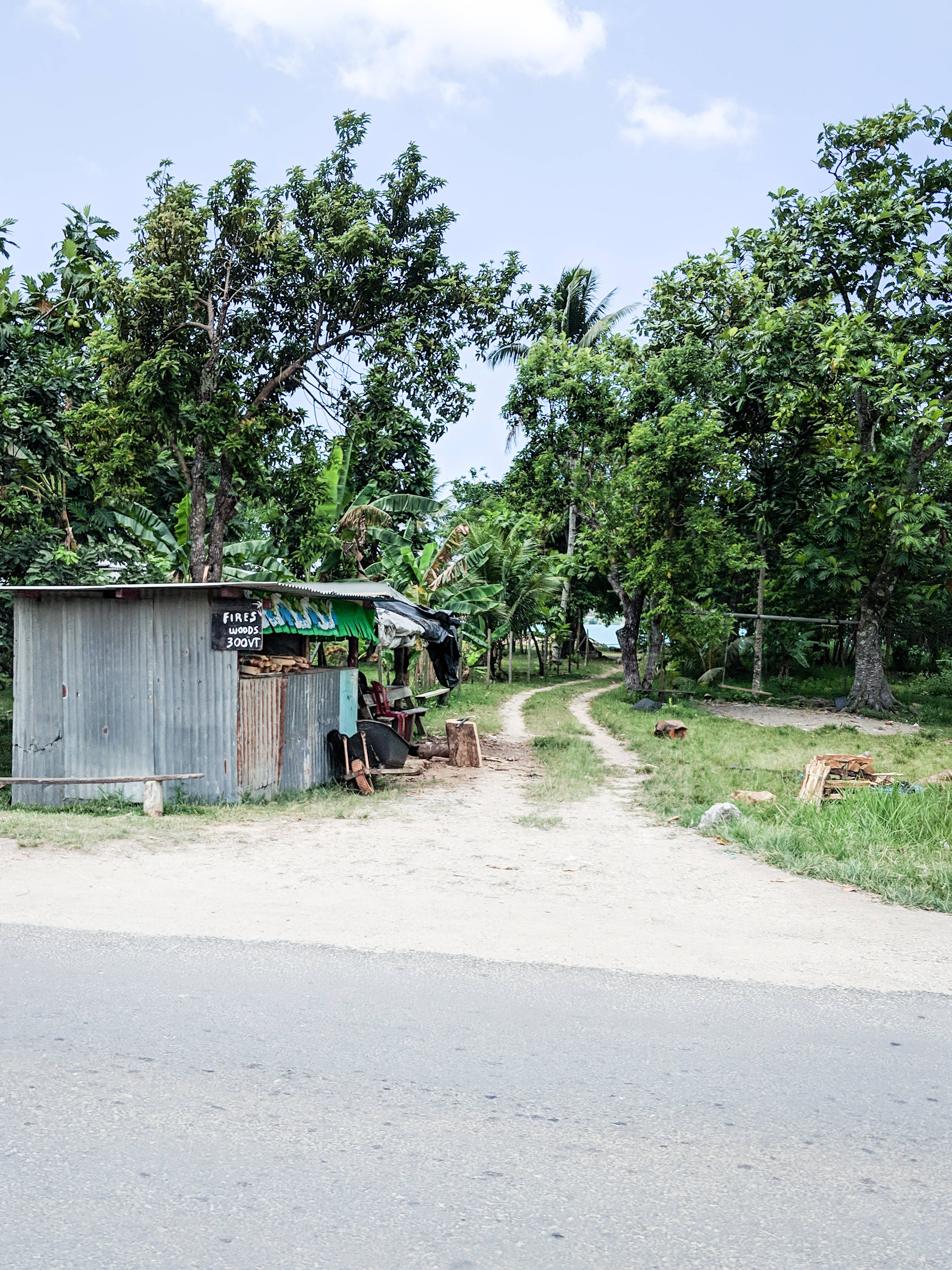 Vanuatu 桌布 壁紙 — 一間帶有綠色遮陽篷的鄉村路邊小屋，旁邊是一條蜿蜒穿過茂密綠樹的碎石小路，上方是明亮的藍天。