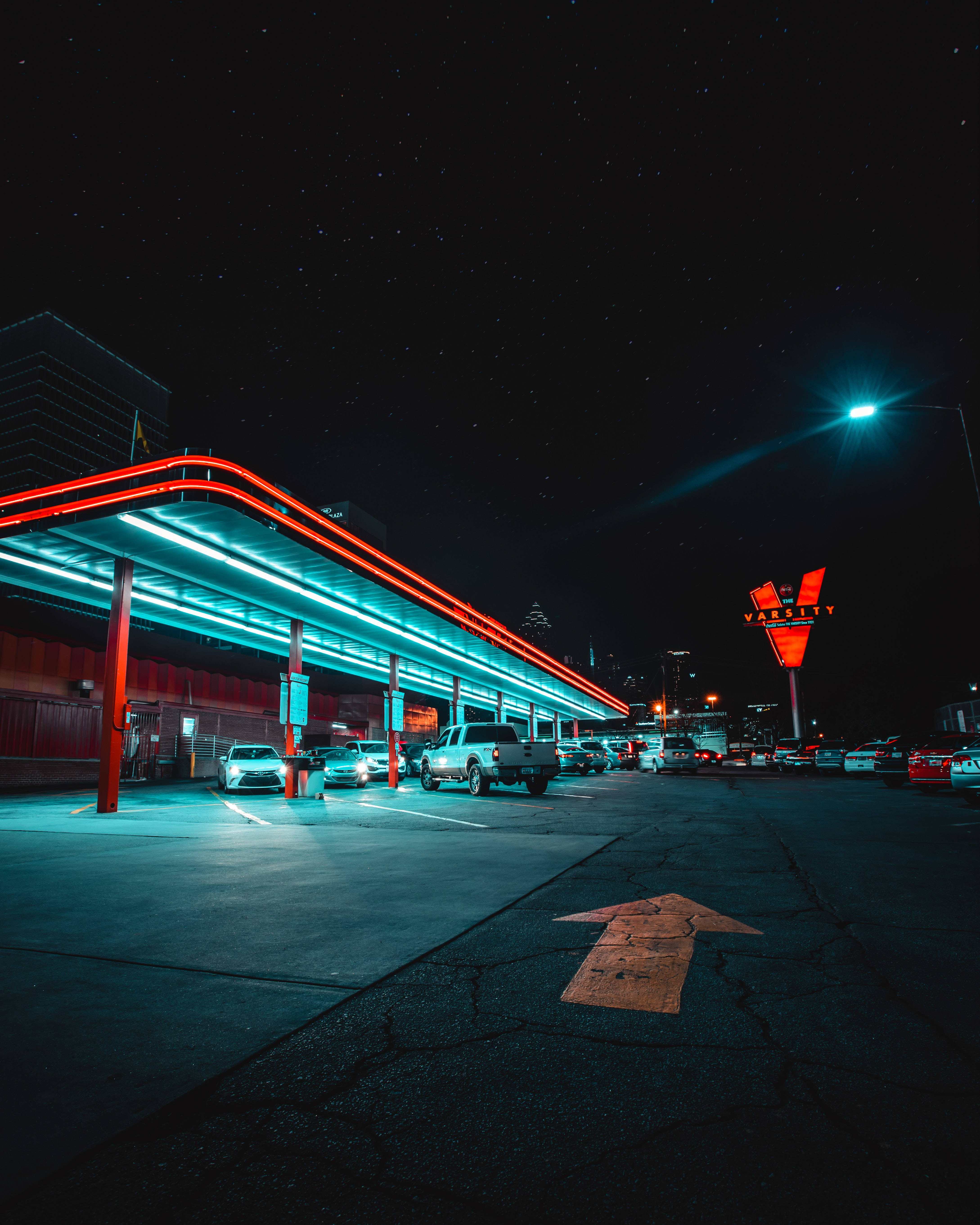 霓虹車 桌布 壁紙 — 一間復古加油站在繁星夜空下閃耀，霓虹燈將鮮豔的紅色和藍色投射在停放的汽車和路面上。