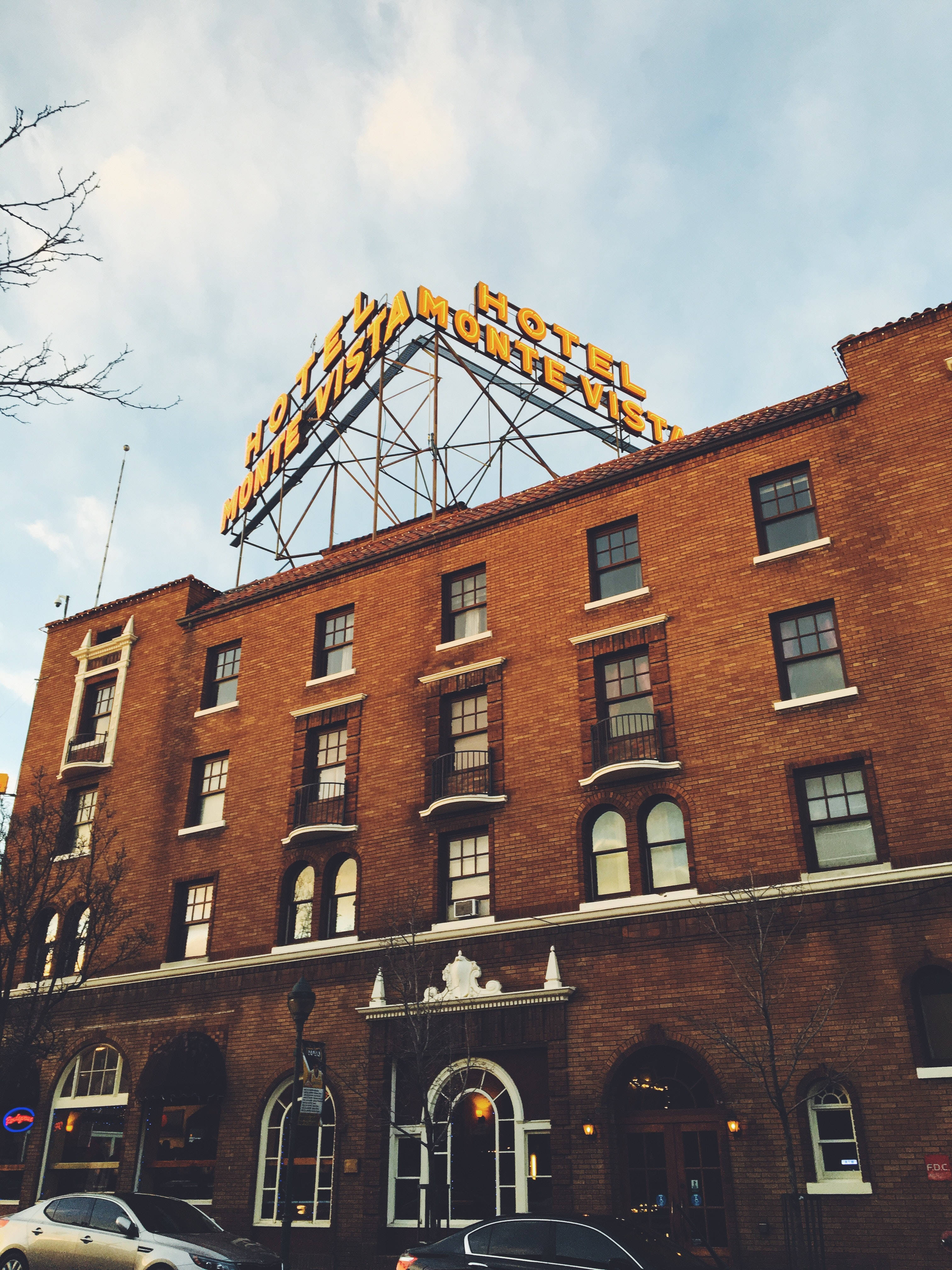 Hotel 桌布 壁紙 — 一間復古磚砌酒店，帶有一個大型發光招牌，上面寫著「HOTEL MONTE VISTA」，背景是部分多雲的天空。