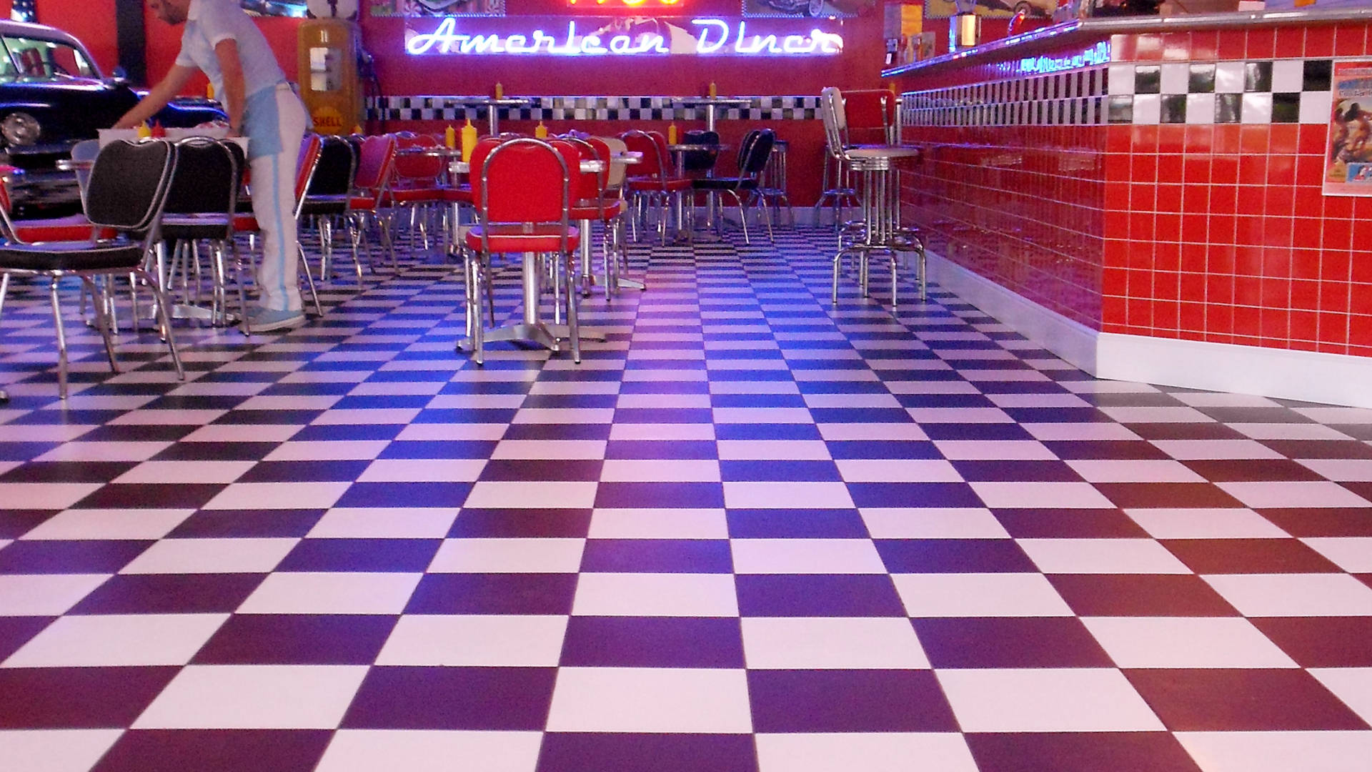 Diner 桌布 壁紙 — 一間復古風格的餐廳，擁有搶眼的格紋地板、紅色卡座，以及在明亮燈光下溫暖發光的霓虹招牌。