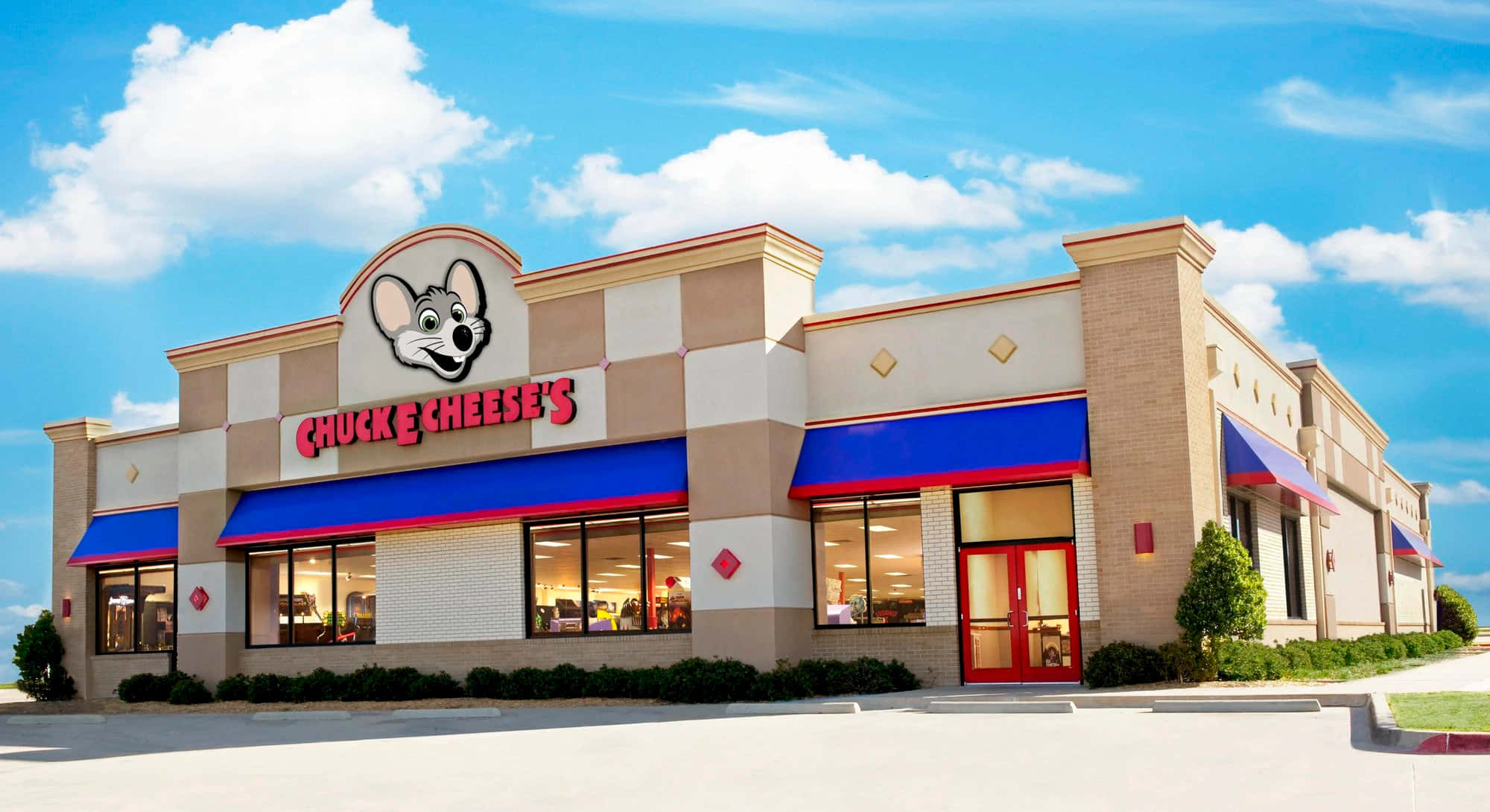 查克芝士 桌布 壁紙 — 一間明亮的Chuck E Cheese's餐廳，設有藍色遮陽篷和紅色門，位於陽光明媚、雲朵蓬鬆的天空下。