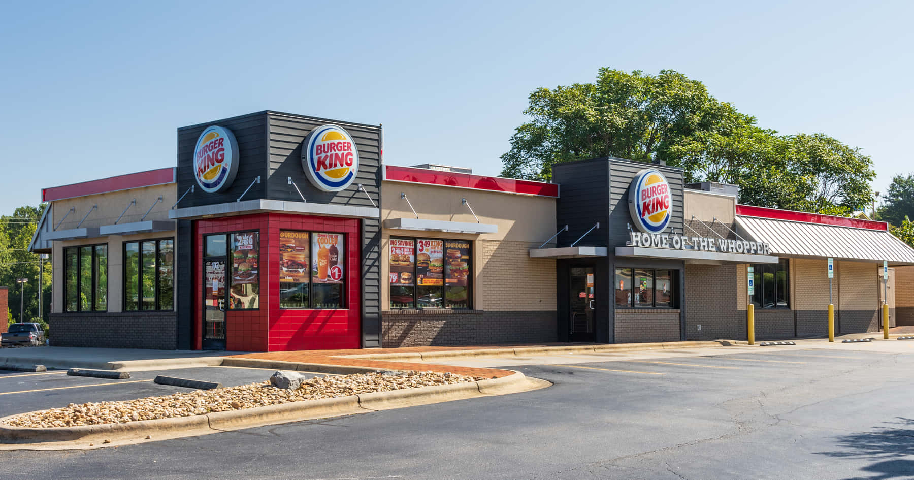 Burger King 桌布 壁紙 — 一間明亮的漢堡王餐廳，帶有紅色點綴和大窗戶，在晴朗的藍天下。