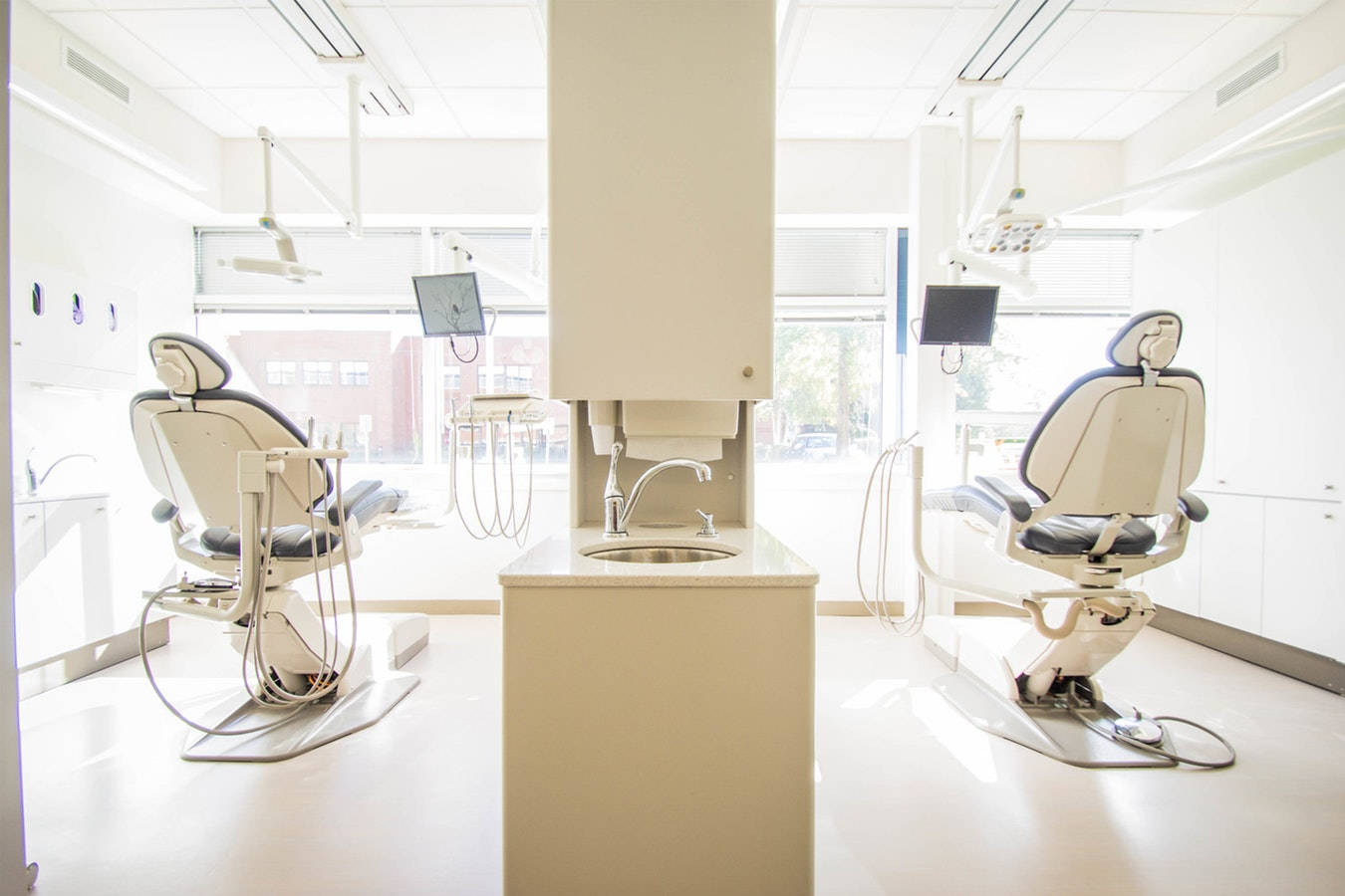 Dentistry 桌布 壁紙 — 一間明亮的現代牙科診所，設有兩張白色躺椅，面向中央洗手台和讓自然光線透入的大窗戶。