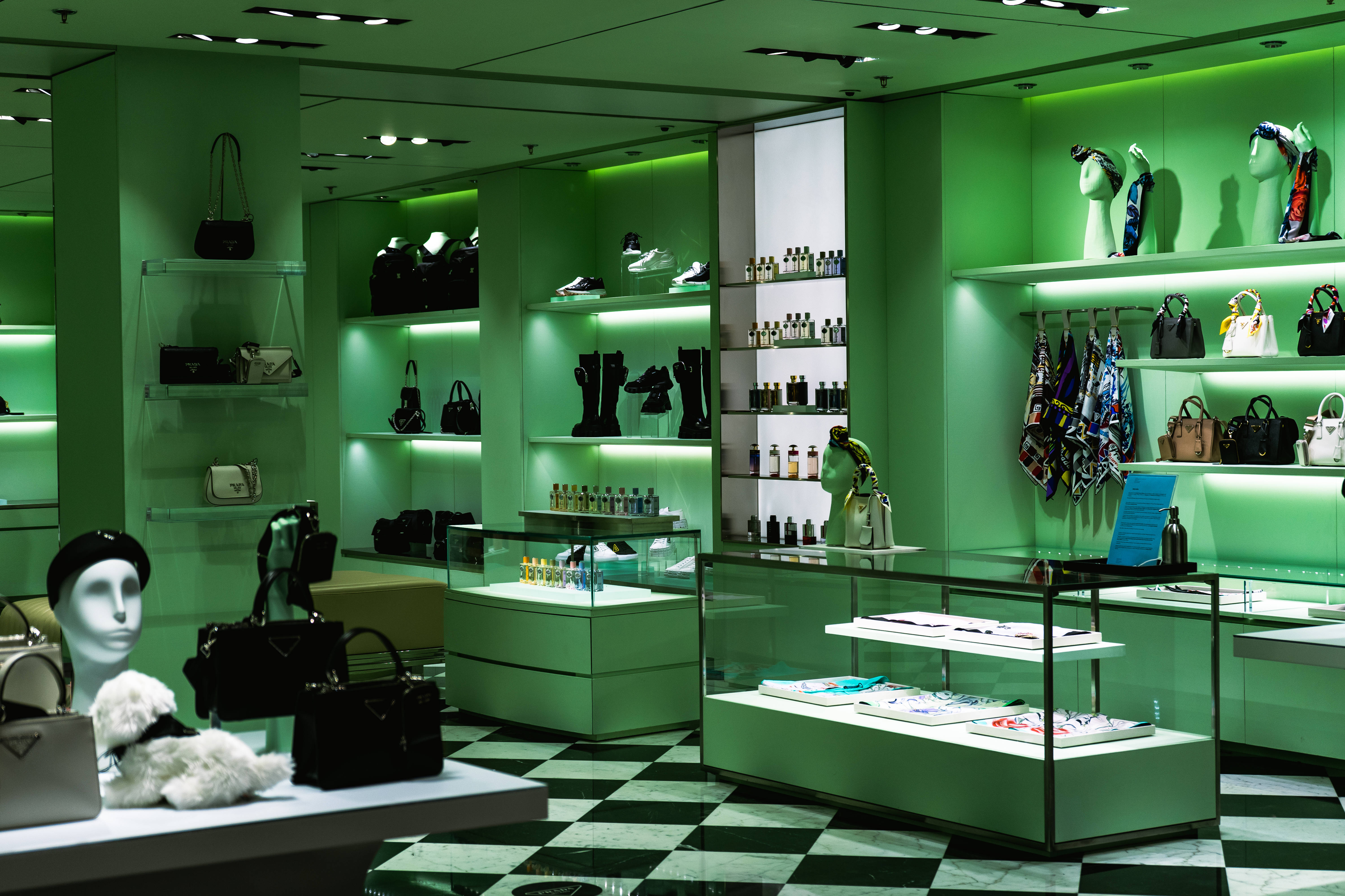 Prada 桌布 壁紙 — 一間時尚奢華精品店沐浴在充滿活力的綠色燈光中，在玻璃架和模特兒上展示手提包、鞋子和配件。
