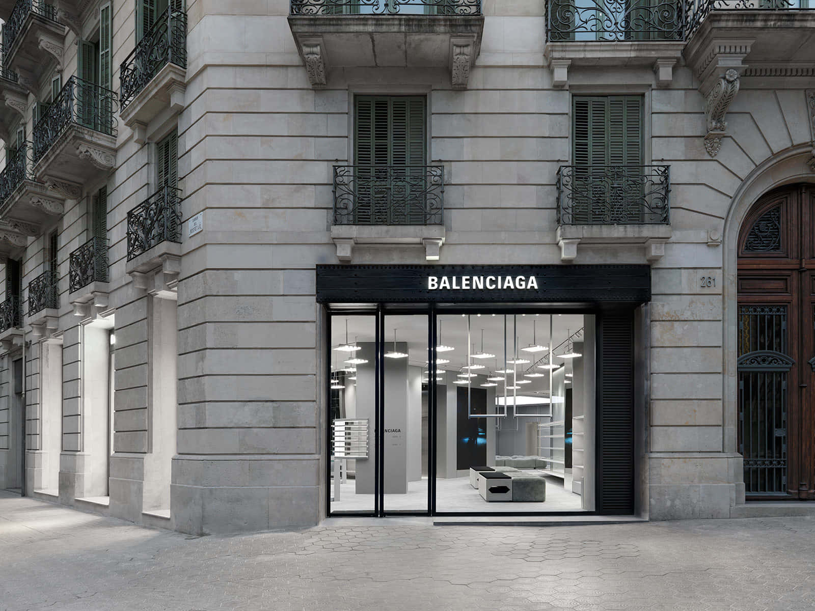 巴黎世家 桌布 壁紙 — 一間時尚的Balenciaga商店，設有黑色框玻璃門和極簡主義的室內照明，背景是帶有華麗陽台的歷史石建築。