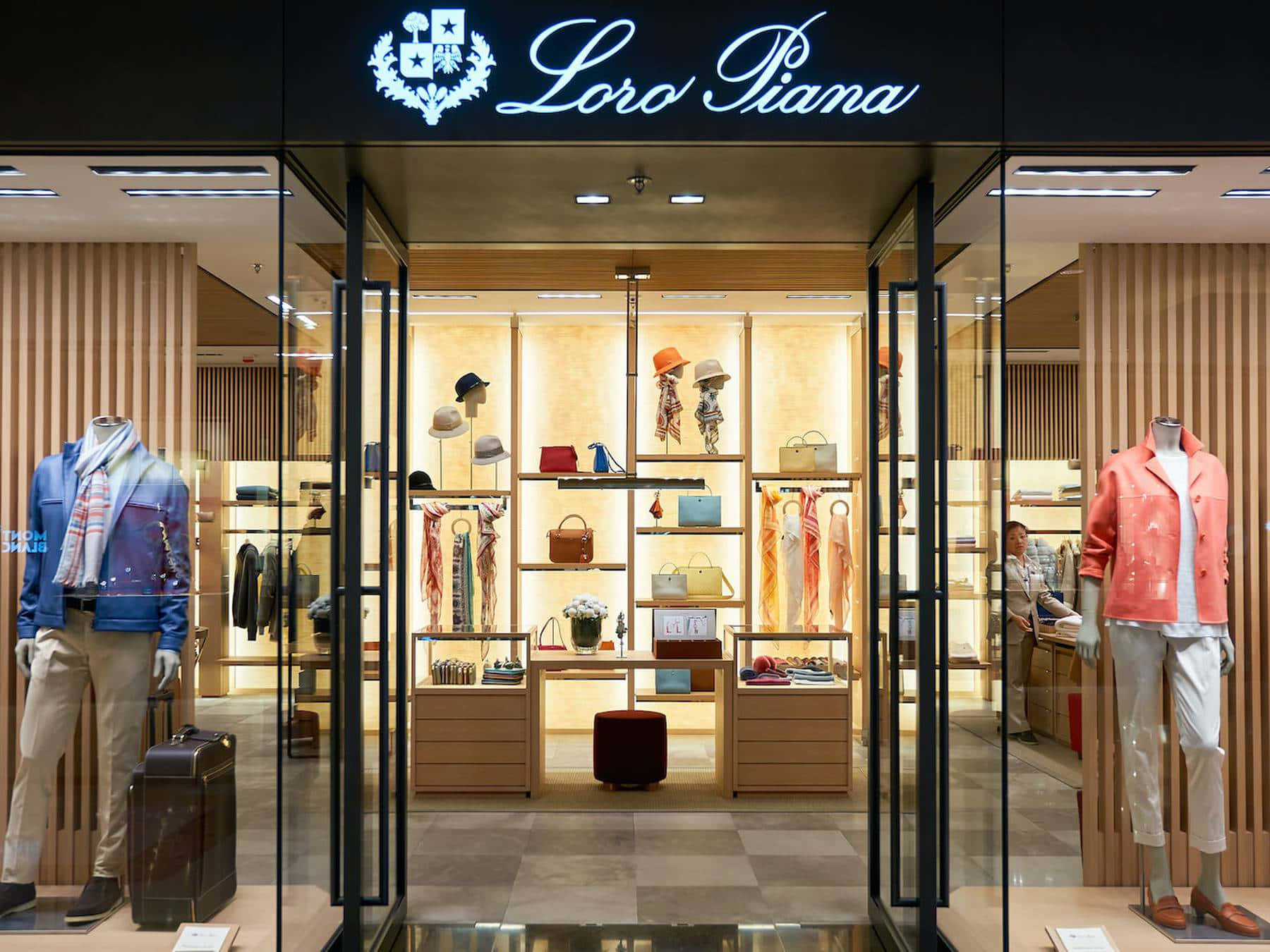 Store 桌布 壁紙 — 一間時尚的Loro Piana精品店，玻璃門展示著穿著訂製服裝的人體模型和豪華配飾架，在溫暖的燈光下。
