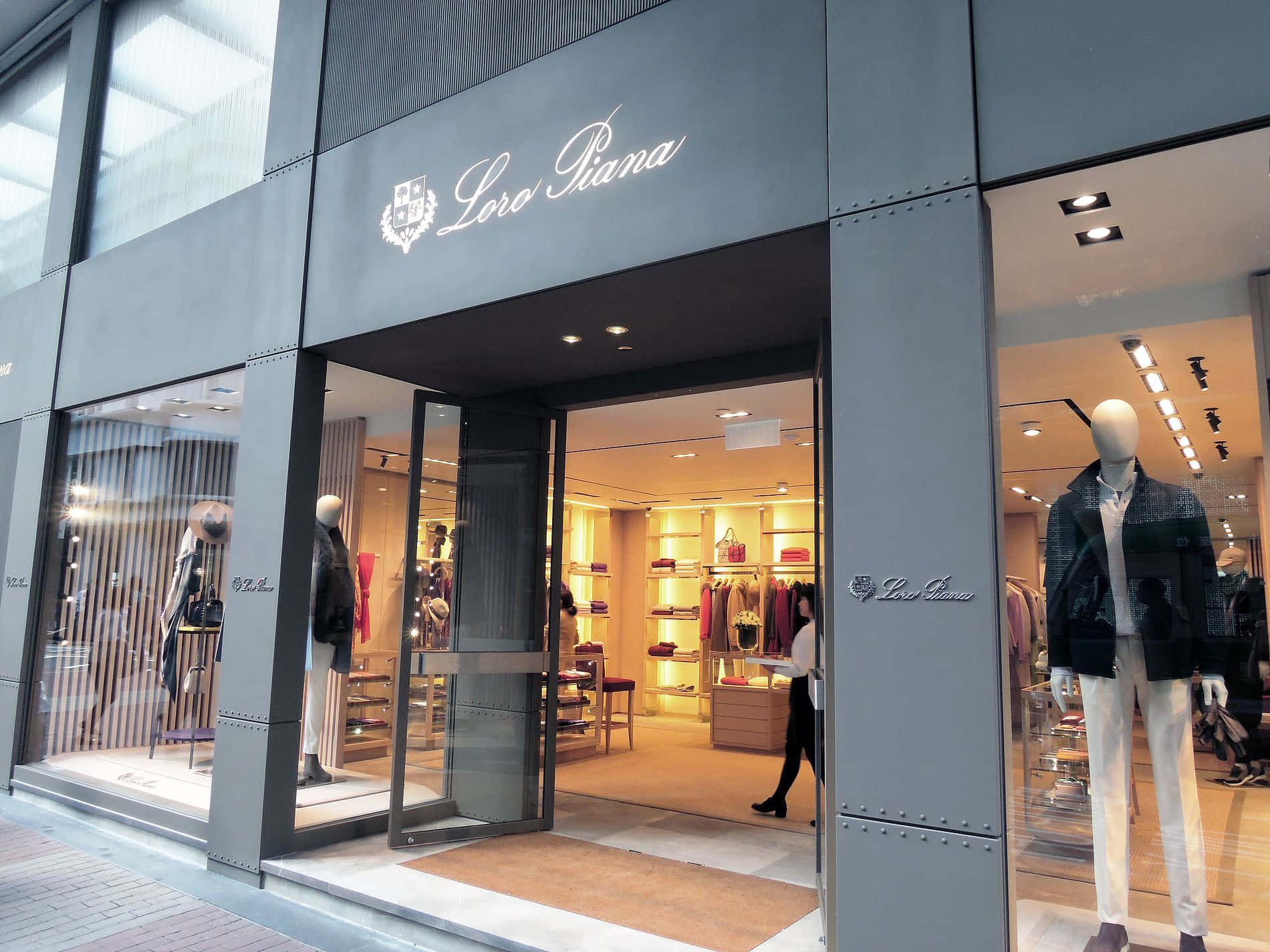Shopping 桌布 壁紙 — 一間時尚的Loro Piana精品店，設有玻璃門和模特兒，在溫暖的室內燈光下展示奢華男裝。