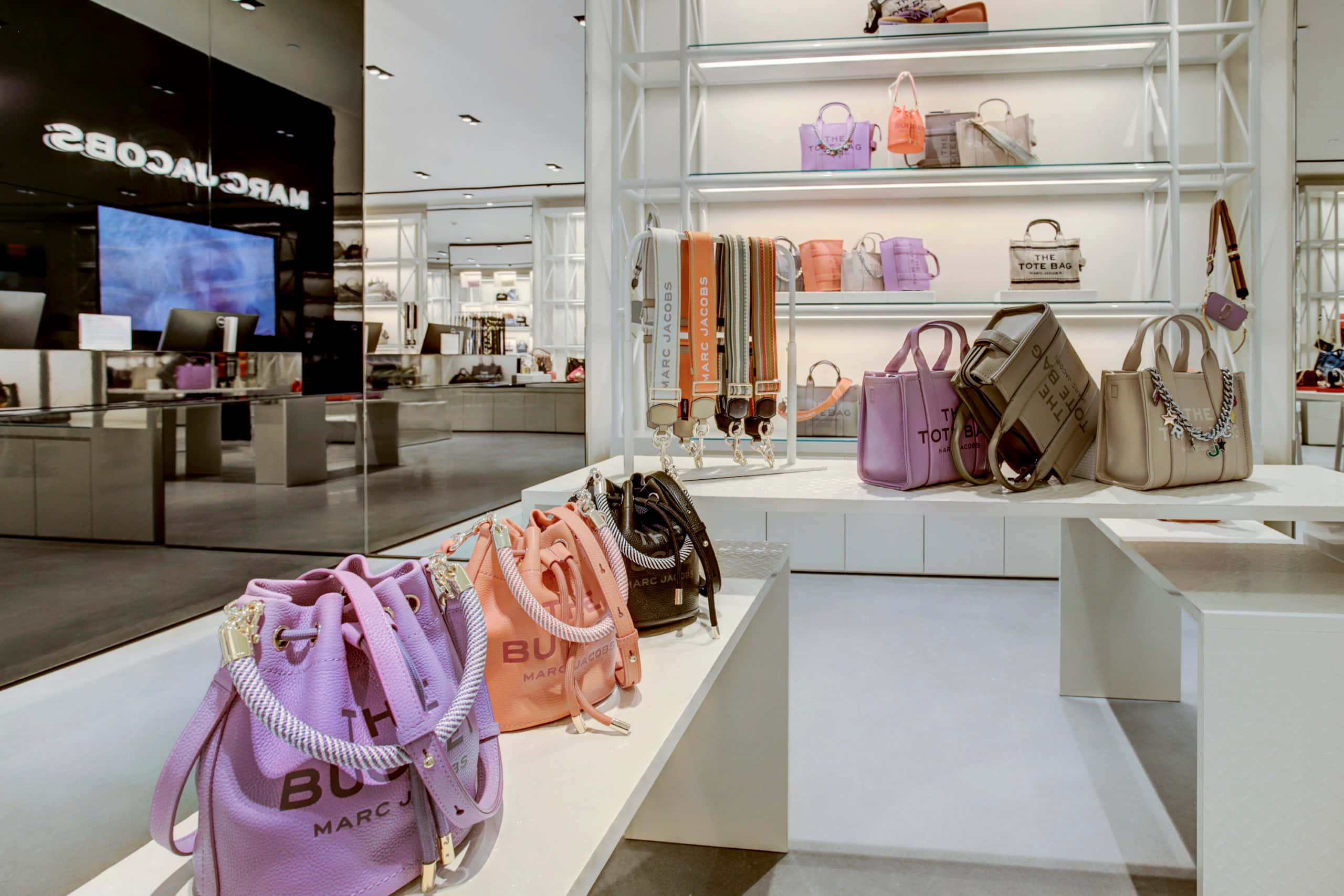 馬克·雅可布 桌布 壁紙 — 一間時尚的Marc Jacobs商店在明亮的燈光下，於白色貨架和櫃檯上展示色彩繽紛的手袋。