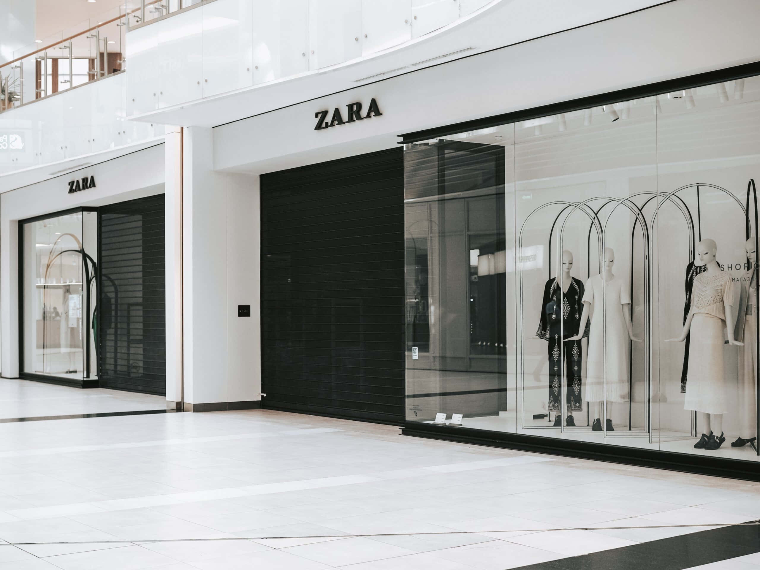 Zara 桌布 壁紙 — 一間時尚的Zara商店，配有黑色百葉窗和玻璃窗，在明亮的現代購物中心內展示穿著簡約黑白服裝的人體模型。