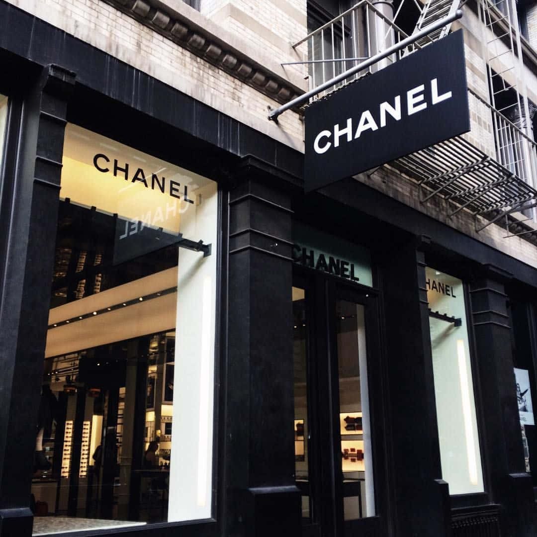 Chanel 桌布 壁紙 — 一間時尚的黑色 Chanel 精品店，櫥窗亮著燈，在雨中的城市背景下展示奢侈品。